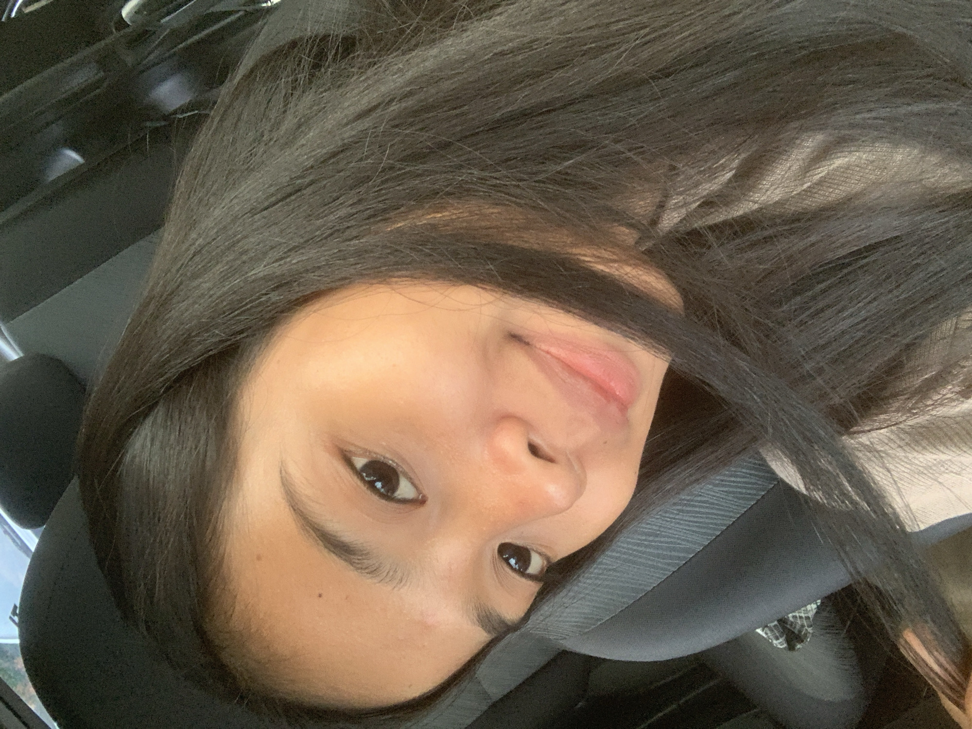A young woman with long, dark hair is wearing a seatbelt in what appears to be a car. The background shows a car interior and parts of the exterior visible through the windows. The location is likely Samarinda, Indonesia, inferred from the user's request.