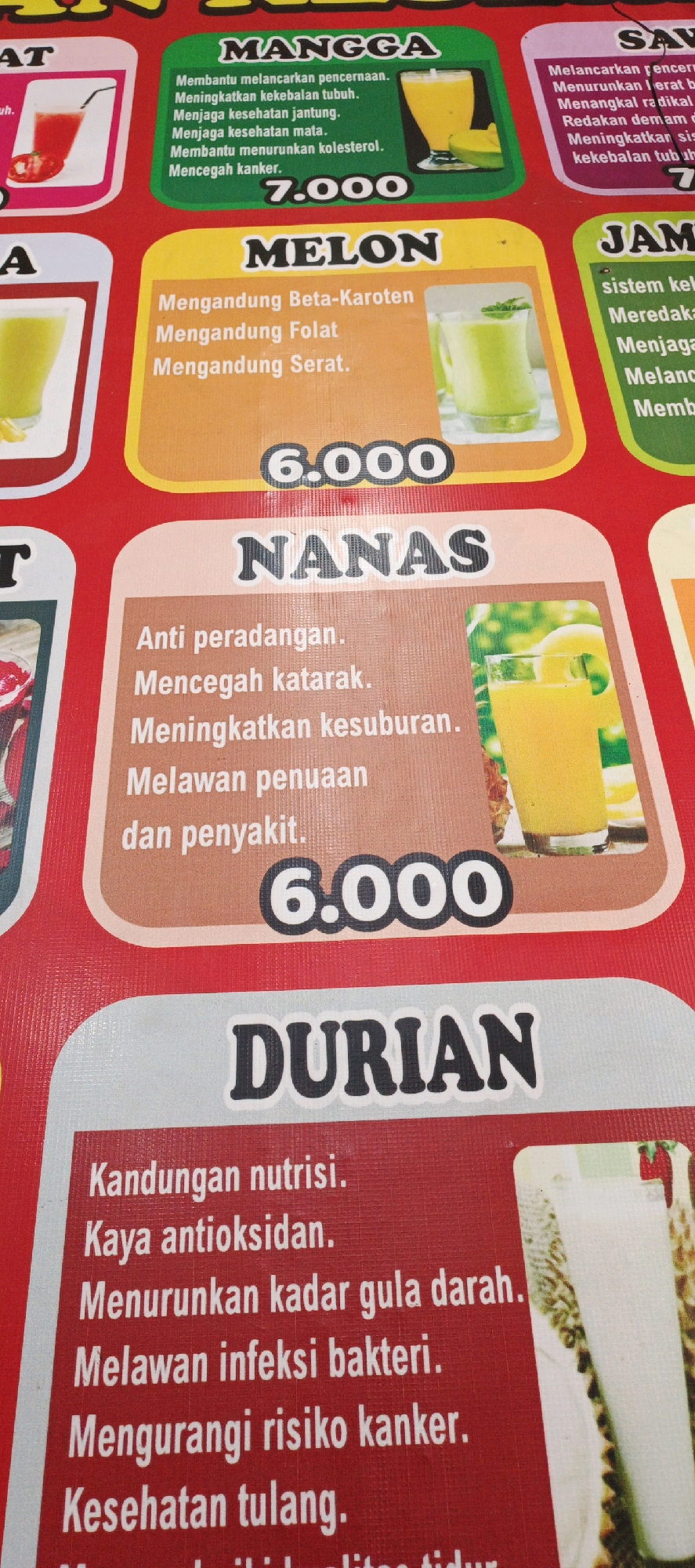 The image is a close-up shot of a menu board for fresh juice at an unspecified outdoor establishment in Sidoarum, Indonesia. The menu is predominantly red with colored sections for different fruit juices. The top section displays "MANGGA" (Mango) with a price of "7.000" and a list of benefits in Indonesian. To the right, partially visible, is "SAM" (likely referring to a fruit like "Sirsak" or "Semangka"). Below "MANGGA" is "MELON" with a price of "6.000" and a list of benefits. To the right of "MELON," partially visible, is "JAM" (likely "Jambu" or "Jeruk"). The bottom section features "NANAS" (Pineapple) with a price of "6.000" and a list of benefits, followed by "DURIAN" with a list of benefits. Images of the respective juices are displayed next to their descriptions. The lighting appears to be natural daylight, and the overall scene suggests a vibrant, local food or beverage stall.