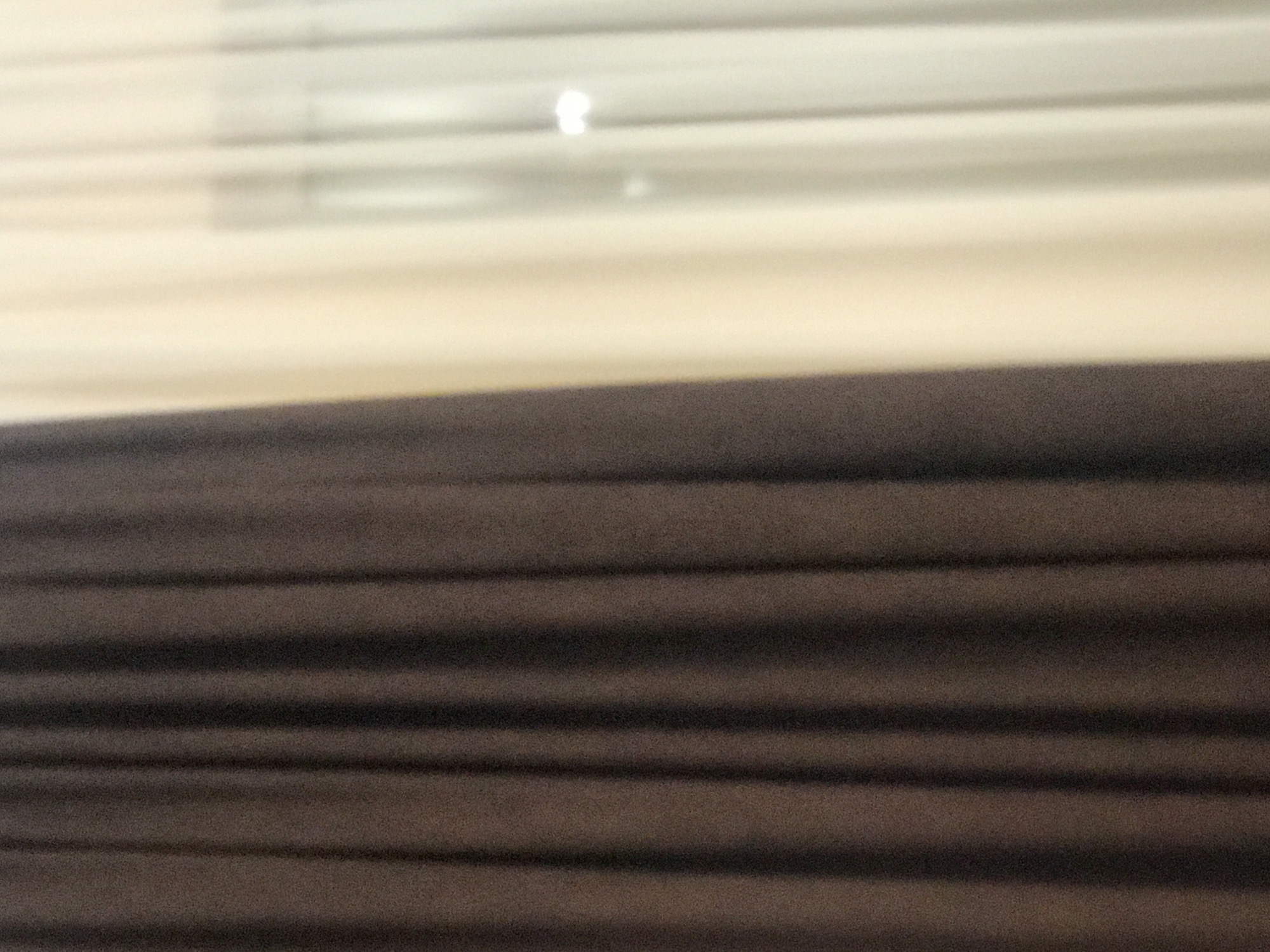 The image shows a close-up view of closed brown horizontal blinds. Above the blinds, there is a blurred view of white blinds. There is no indication of the location being Yerevan, Armenia, nor are there any people, actions, or interactions visible in the image.
