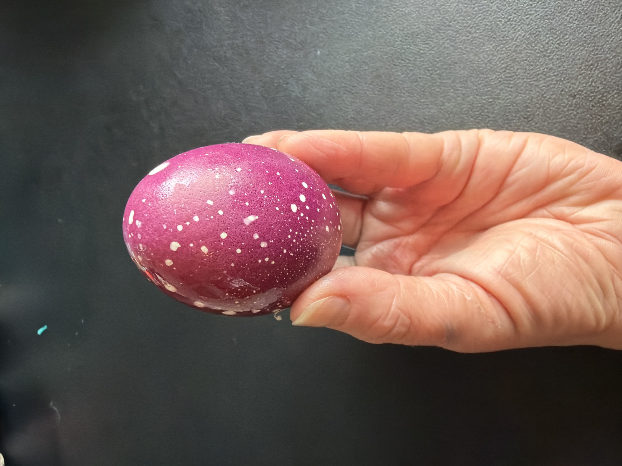 A hand is holding a purple, speckled sphere. The background is a dark gray surface. The scene does not appear to be in Murino, Russia based on the visual information provided.