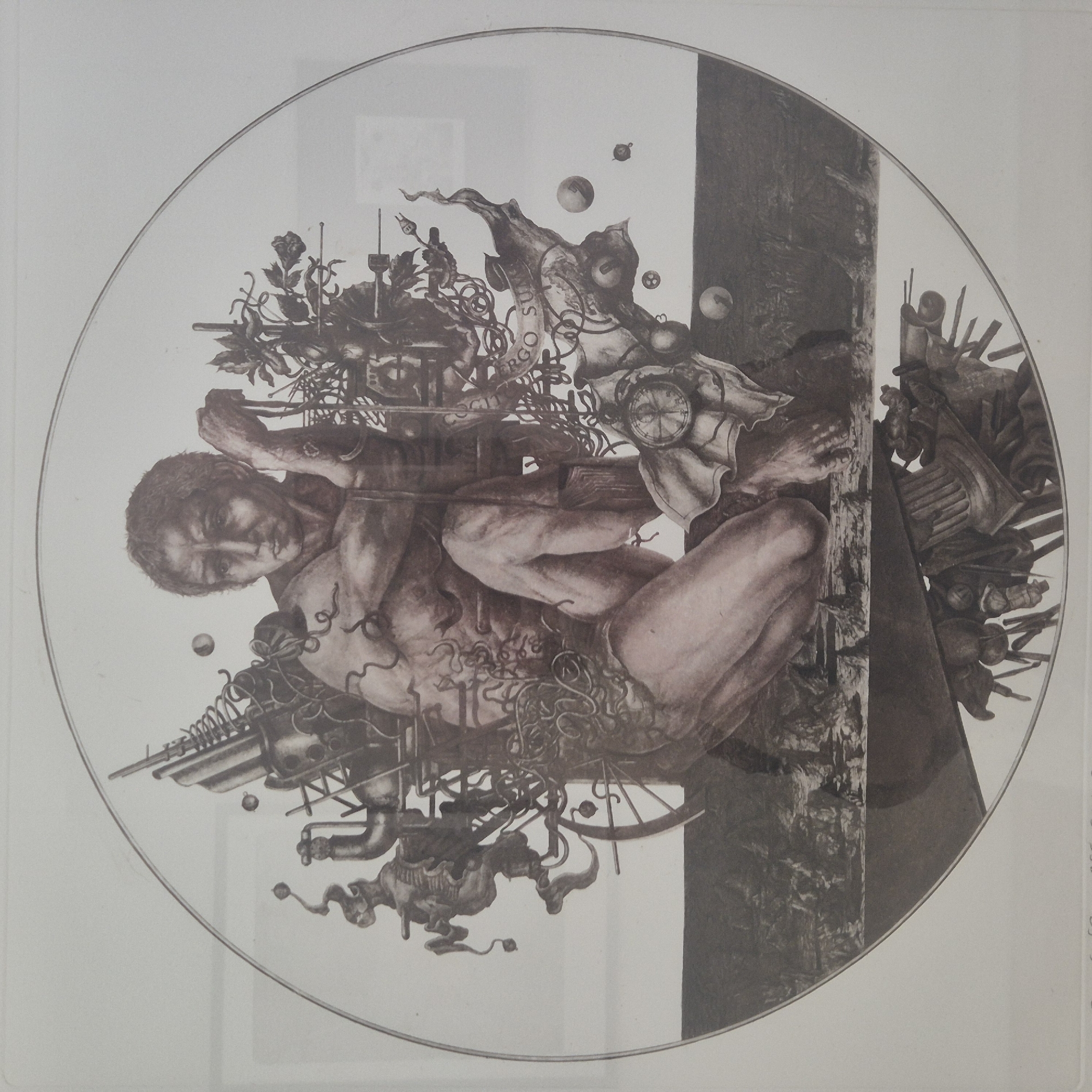 This is a black and white, circular artwork depicting a mythological or allegorical scene. The central figure is a muscular, pale-skinned man, seated and leaning on his right arm, with a somber expression. He appears to be partially entwined with a complex arrangement of mechanical and organic elements, including gears, pipes, coils, and what appears to be thorny vines or branches. A pocket watch is visible near his left leg, and a spool or bobbin-like object is on his right arm.
Surrounding the man are various surreal and symbolic objects. To his left, there is a contraption resembling a stylized horse or mythical creature made of mechanical parts. To his right, plants with roses and other foliage are intermingled with mechanical structures. Several spheres or orbs, some with numbers (like 1, 2, and 3), are floating around the composition. A banner-like element with the inscription "ERGO SUM" is visible behind the man.
The lower portion of the artwork is divided into two distinct horizontal bands. The upper band depicts a dark, textured landscape with rocky formations, possibly a desolate or post-apocalyptic scene. The lower band, visible at the very bottom, shows a jumble of intricate, dark mechanical or architectural fragments, some resembling gears, columns, and perhaps insect-like appendages.
The artwork is presented within a white border, and a faint circular line demarcates the outer edge of the art itself. The image lacks any specific indication of location within the city of Vitsebsk, Belarus, or any other geographical context. It is a stylized, symbolic, and surreal composition.