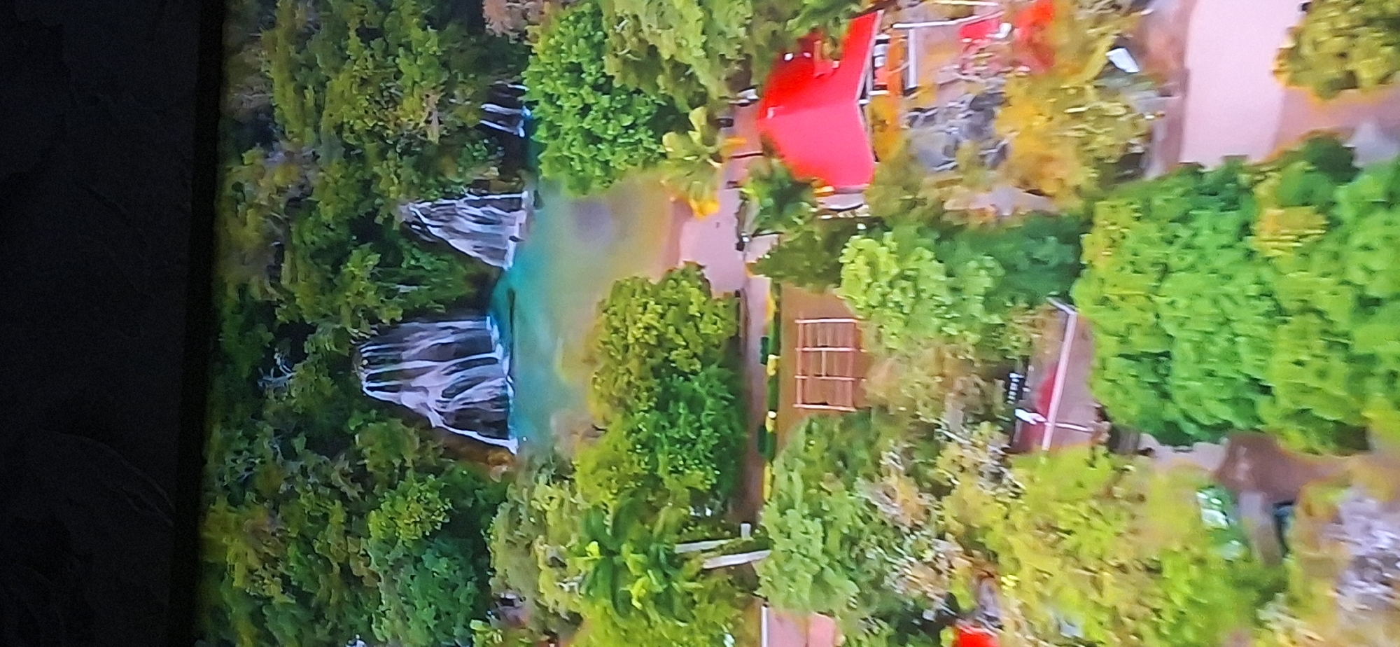 The image is an aerial view of a lush, green landscape with waterfalls and a body of water in the background. In the foreground, there are trees, a building with a red roof, and some pathways. The image quality is poor and pixelated, making it difficult to discern specific details. There is no discernible information within the image to suggest any connection to Bila Tserkva, Ukraine.