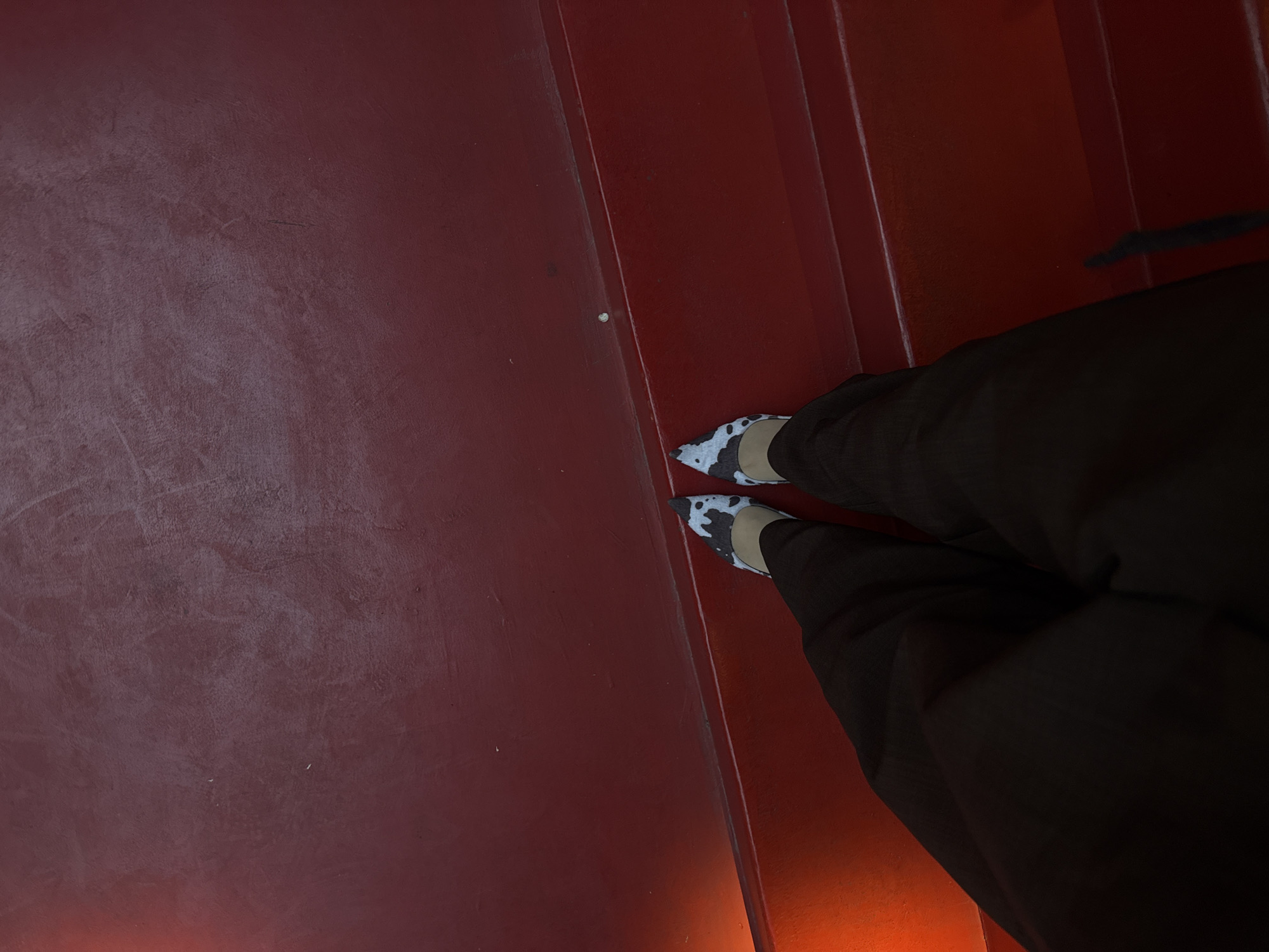 A person is standing on a red staircase, wearing black pants and white and black patterned shoes. The floor is also red. There is no indication of this scene being in Yerevan, Armenia.