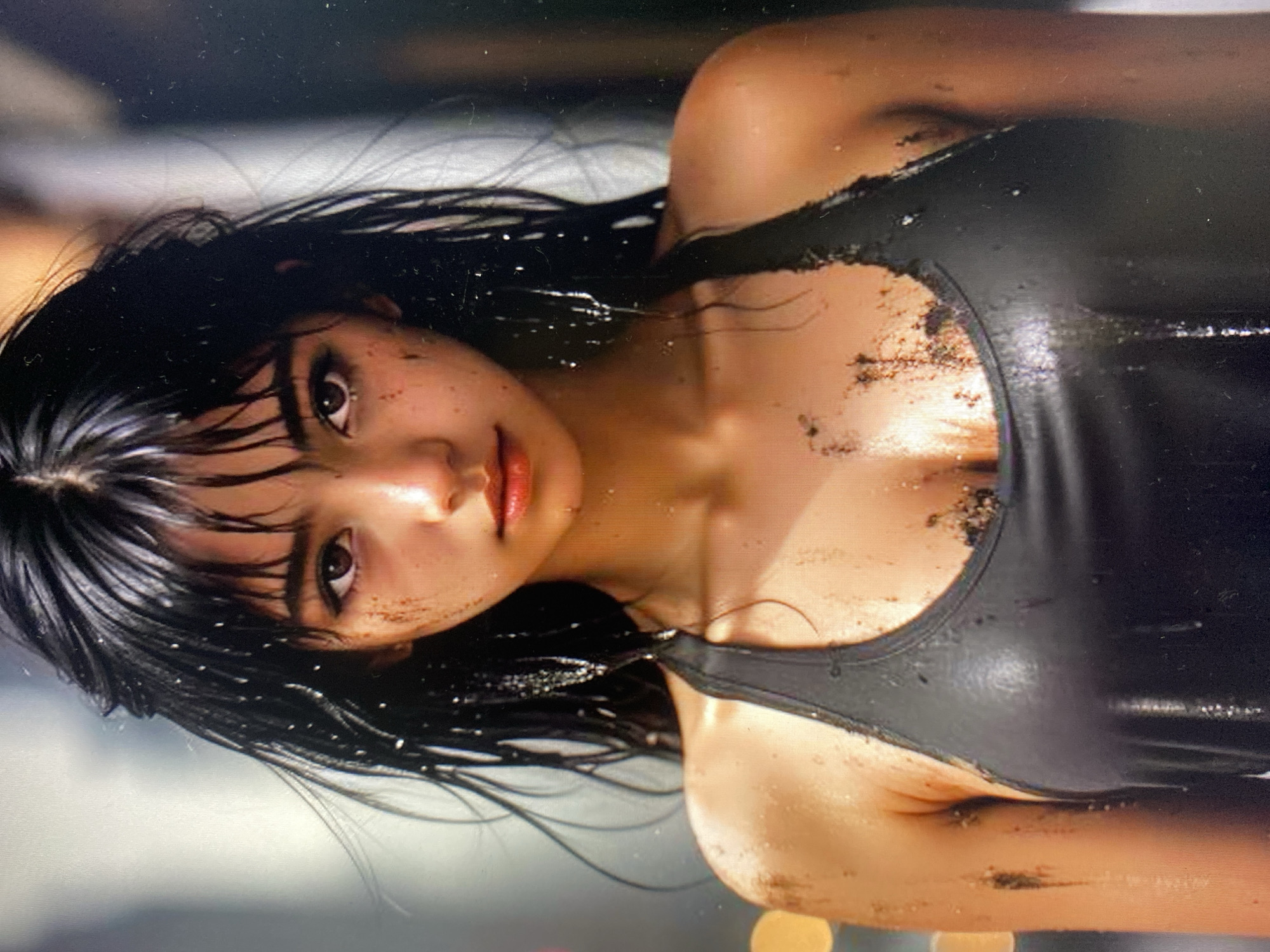A medium shot photograph shows a young East Asian woman with wet, dark hair and dirt smudges on her face, neck, and chest. She is wearing a black tank top, which appears damp and also has dirt on it. Her gaze is directed at the viewer, and her expression is neutral. The background is blurred and indistinct, with out-of-focus bokeh lights suggesting an urban or indoor setting. The lighting is dramatic, highlighting the textures of her skin and hair, and the overall impression is one of grit and resilience. The image does not provide any specific information about the location within the city of Unknown, Unknown, or any particular actions or interactions taking place.
