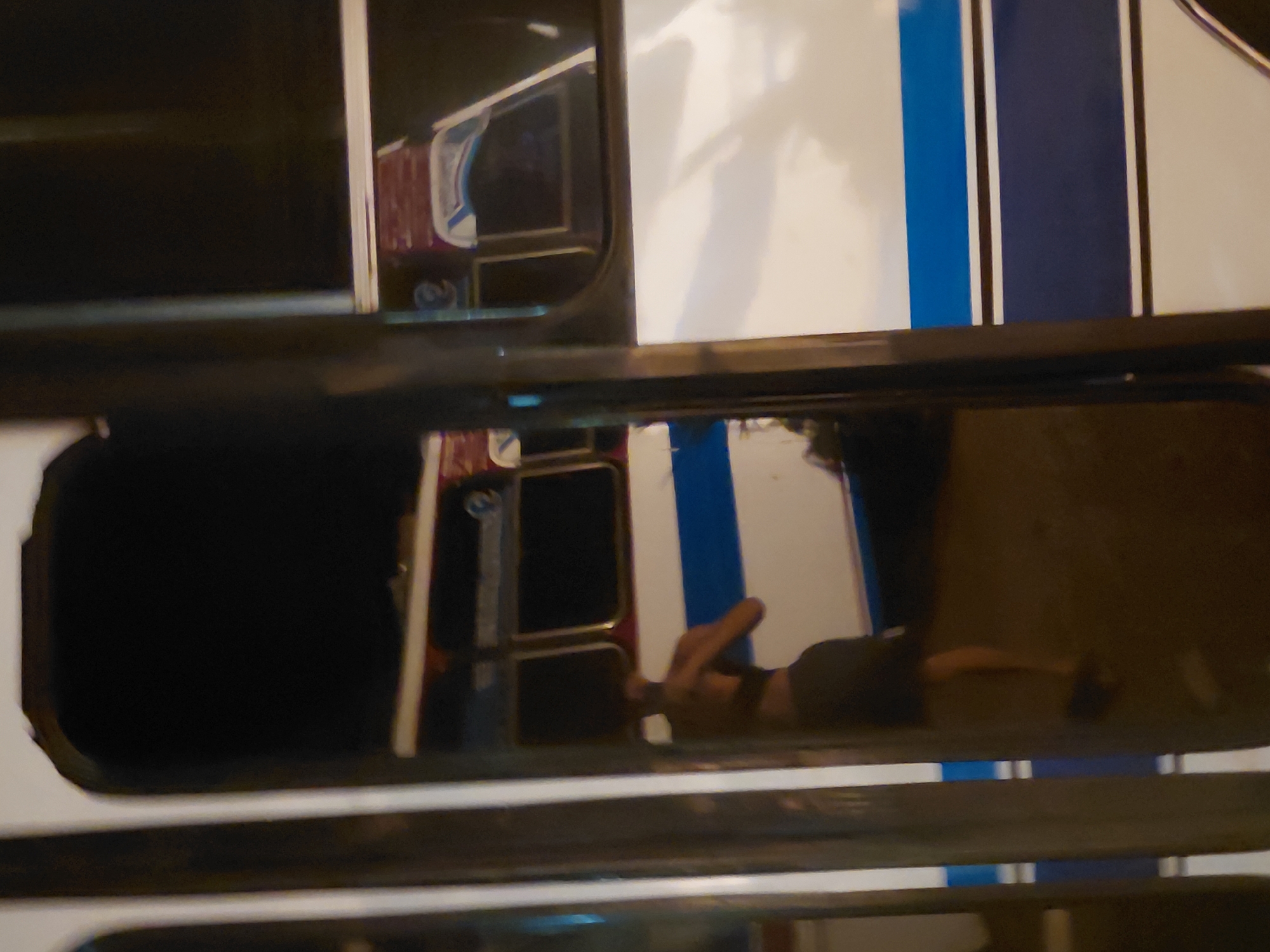 The image shows a person standing next to a bus in what appears to be an outdoor setting at night. The bus has blue and white stripes. The person is partially visible and appears to be wearing dark clothing. The lighting is dim, suggesting it may be nighttime. The image is grainy and out of focus, making it difficult to discern fine details. The location is specified as the city of Santa Ana, Venezuela.