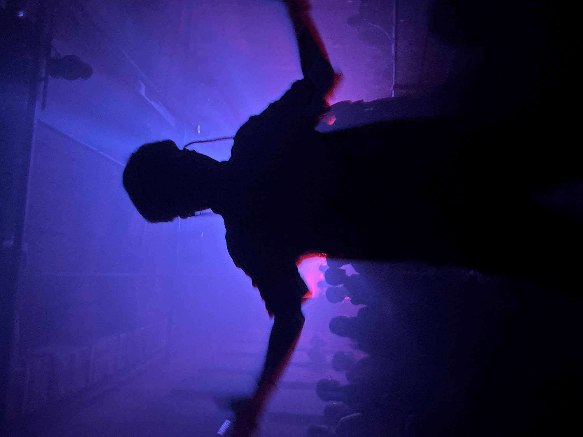 A silhouette of a person stands on a stage illuminated with blue and purple lighting, facing a crowd of people. The scene appears to be a live concert or performance. The location, Buenos Aires, Argentina, is not discernible from the image alone.
