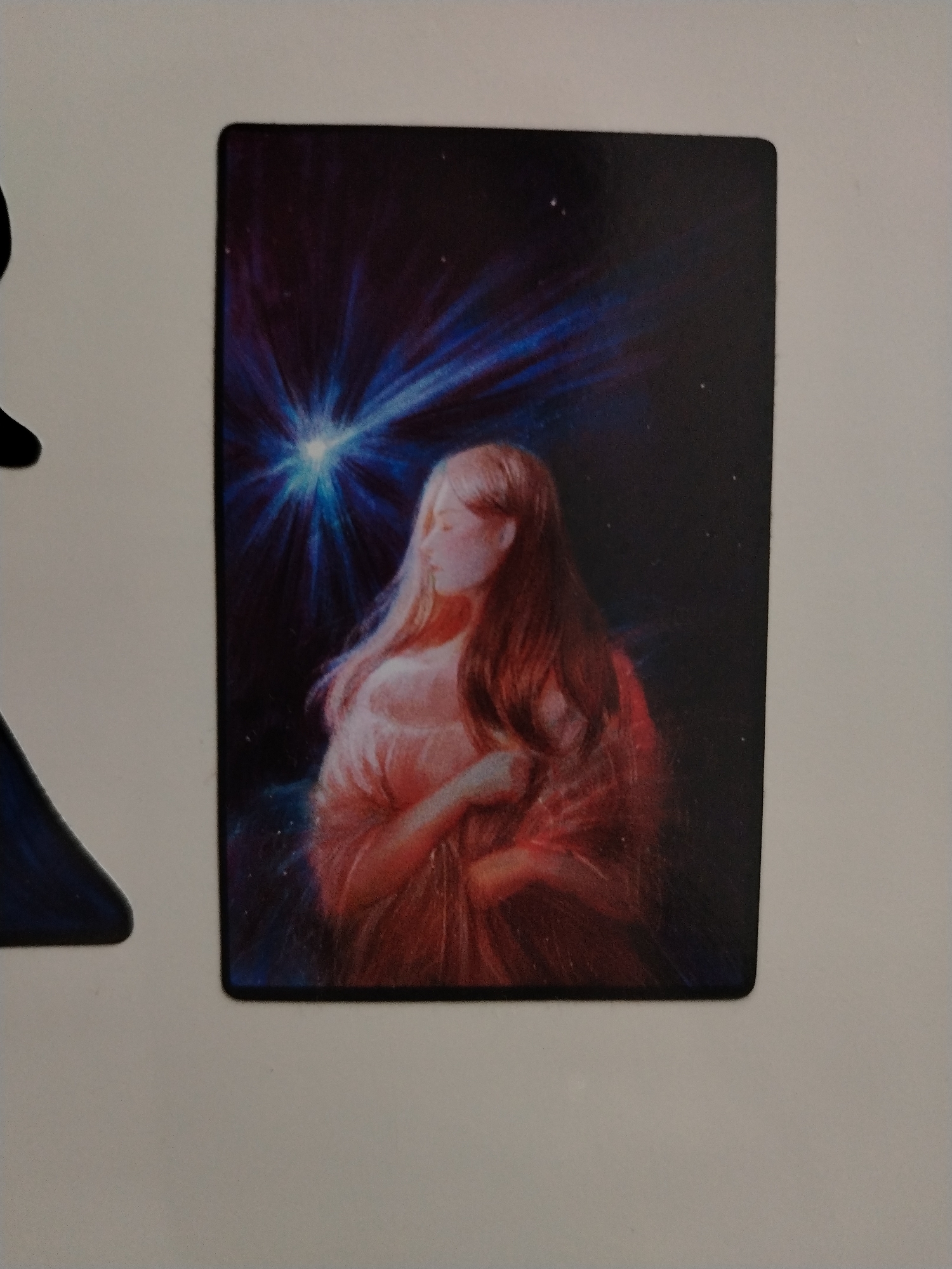 A rectangular image depicts a woman with long, flowing blonde and auburn hair, wearing a peach-colored dress. The woman stands against a dark blue and black background with a bright, radiating blue light source above her. There is no indication of location or cityscape.