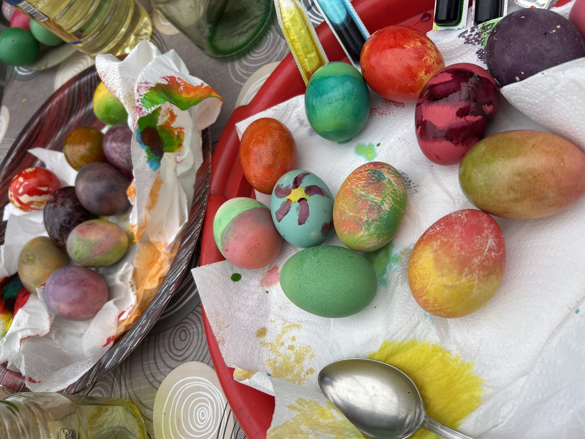 The image shows dyed Easter eggs resting on paper towels inside a tray and a bowl. A spoon is present, and food coloring is visible. The location is most likely a residence or a place associated with Easter celebrations, without specific identifying features related to Zlati Voyvoda, Bulgaria.
