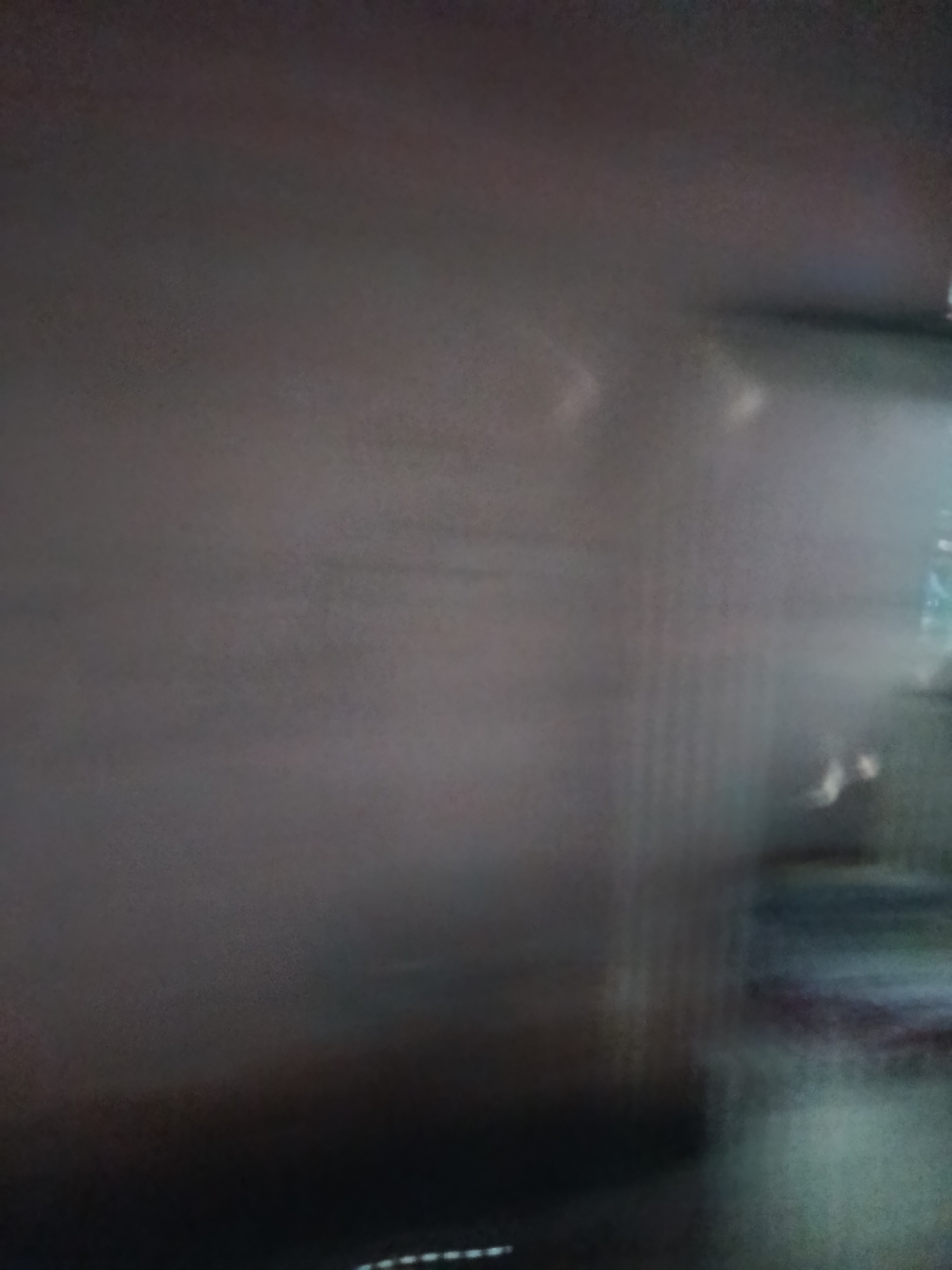 The image depicts a blurry, low-light scene with indistinct shapes and colors. The overall impression is one of a dark, possibly interior space with some ambient lighting. There are vertical lines visible on the right side, suggesting some form of shelving or structured object. Lighter areas appear as smudges or highlights, making it difficult to discern specific details. There is no discernible information within the image to suggest a location in Depok, Indonesia, or any specific context regarding people, subjects, objects, or actions.