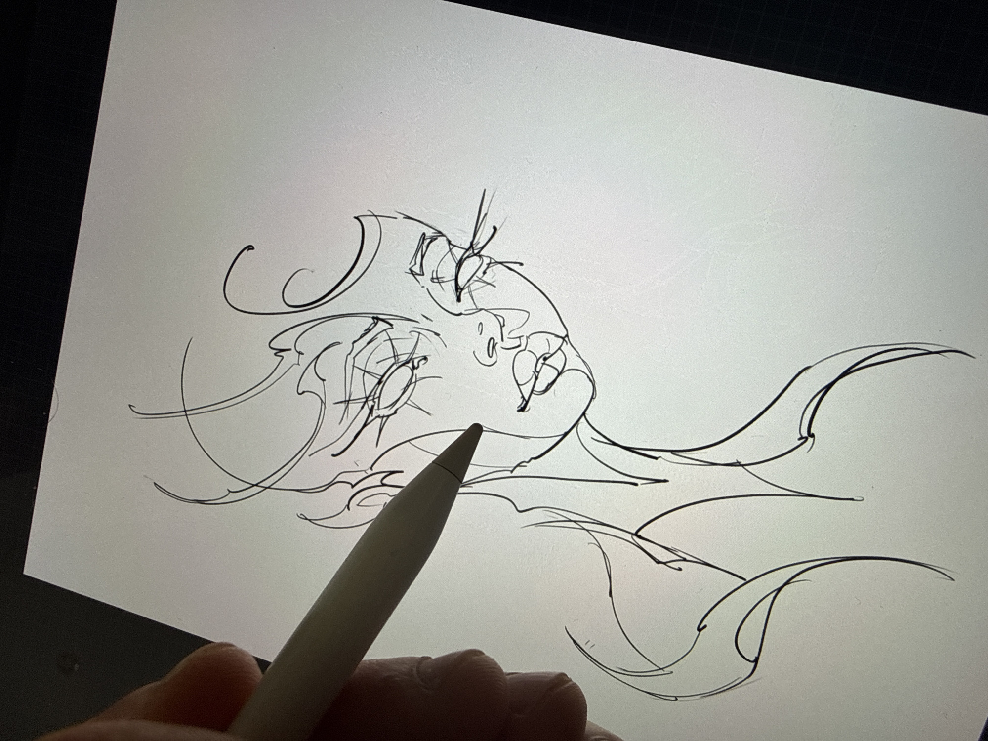 An overhead shot captures a hand holding a white digital stylus, likely an Apple Pencil, actively drawing on a bright screen. The screen displays a stylized, ethereal digital line drawing of a face. The face is depicted with large, closed eyes featuring long eyelashes, and is tilted upwards and to the right, suggesting a dreamy or serene expression. Swirling and flowing lines emanate from and around the face, hinting at hair, fabric, or decorative elements. The artwork is an uncolored outline sketch in black lines against a light grey background, possibly on a tablet or iPad.
The stylus's tip is positioned close to the drawing, indicating the ongoing creation process. The hand holding the stylus has light-toned skin, with fingers slightly curled around the pen. The edges of the digital device are visible as a black frame bordering the light screen. The image focuses on the interaction between the artist's tool and the digital canvas, highlighting the early stages of a creative endeavor. No discernible text is visible within the image.