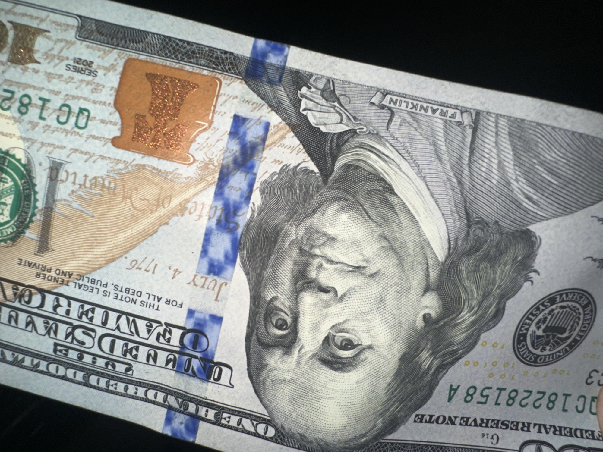 The image shows a close-up of a 2021 series U.S. one hundred dollar bill. Benjamin Franklin's portrait is prominently displayed. The bill features the phrases "Federal Reserve Note," "United States of America," and "One Hundred Dollars." The bill also contains the phrases "This note is legal tender for all debts, public and private," and "July 4, 1776." The serial number "QC18228158 A" is visible. The Treasury seal and the Federal Reserve System seal are also present. The bill has blue security features, and a brown inkwell is visible on the left. The location in Yerevan, Armenia is not visible in the image.