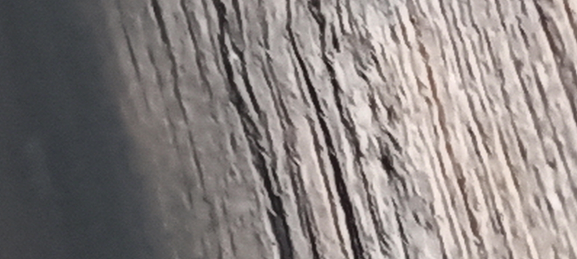 The image shows a close-up of a rough, textured surface, likely a weathered or aged wooden plank or beam. The surface has deep vertical grooves or cracks. There is a smooth, dark surface on the left side. The location, Kryvyi Rih, Ukraine, cannot be verified from the visual content.