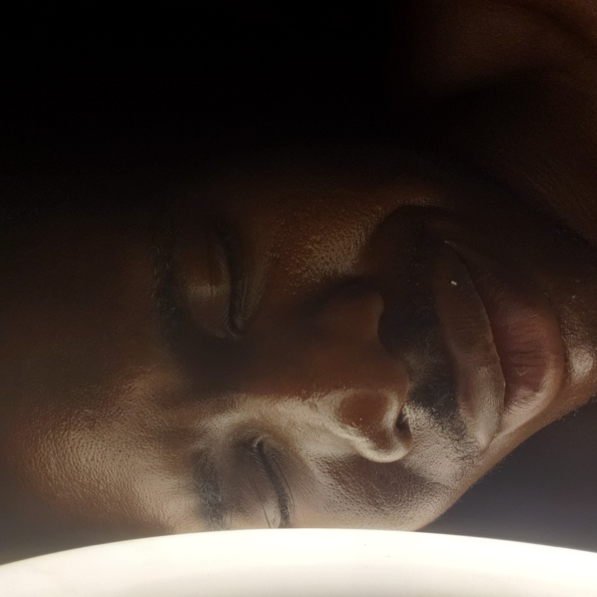 The image depicts a close-up view of a dark-skinned person's face. The person's eyes are closed. The location in the city of Narayi, Nigeria is not detectable.