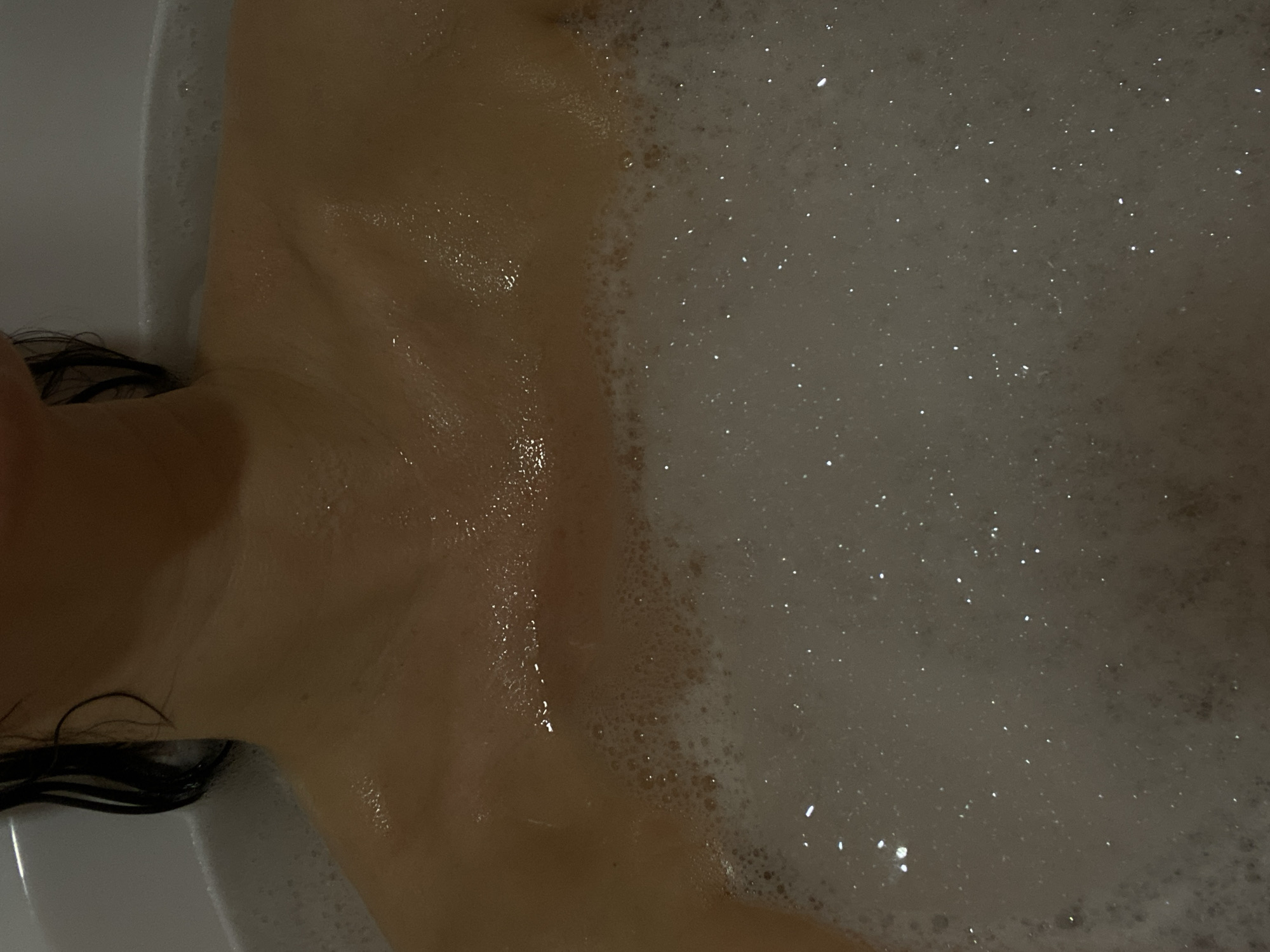 The image shows a person in a bathtub filled with water and bubbles. The individual's chest, neck, and shoulder are visible, along with some dark hair. The setting appears to be indoors in a bathroom. There is no evidence of the image being located in the city of Chaikovsky, Russia.