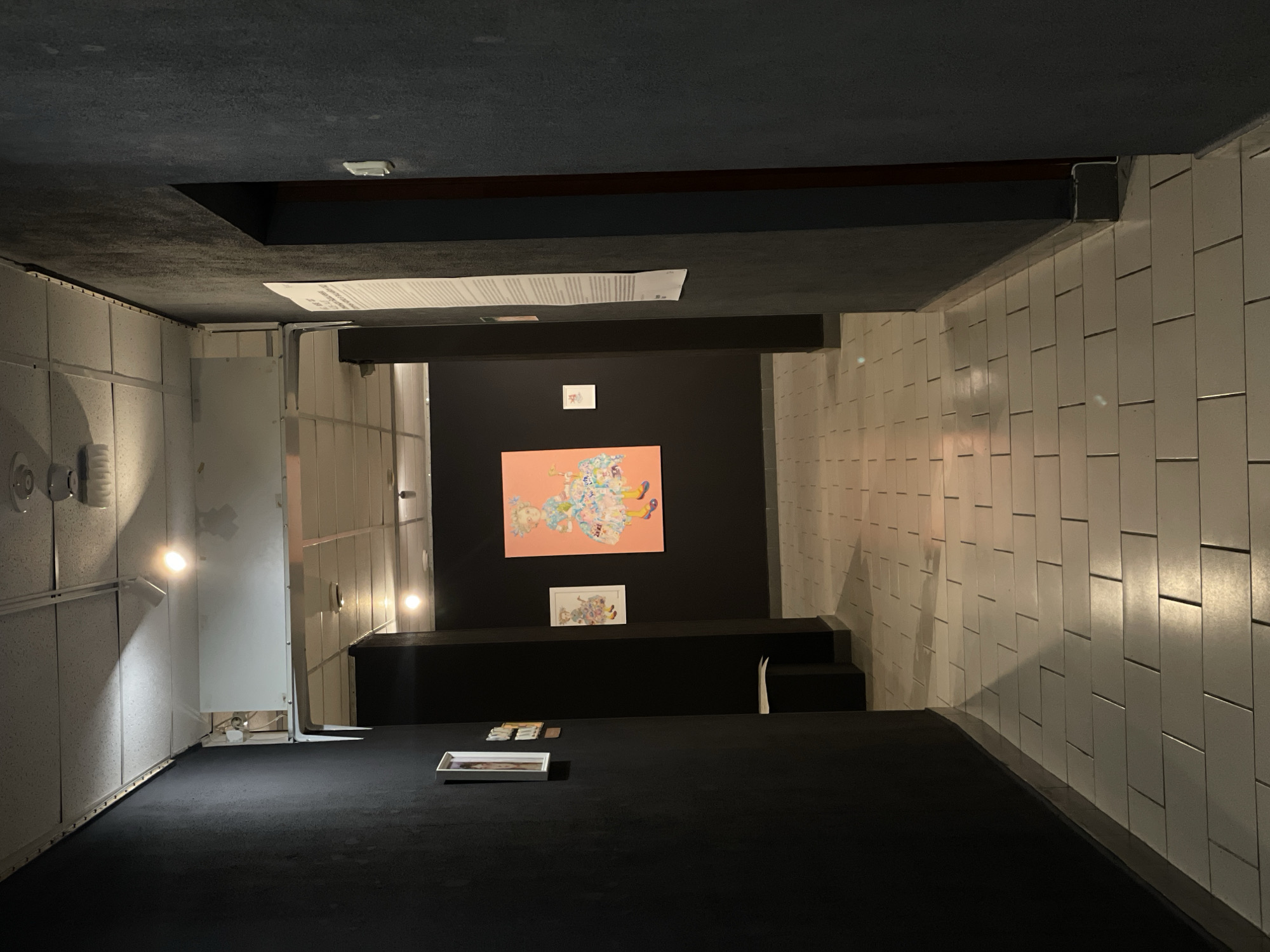 A room in Khimki, Russia is inverted. The walls, tiled in white, appear to be the ceiling, while the dark carpeted floor is above. An artwork on a coral-colored background and a smaller framed piece are displayed on a black wall and platform. A rectangular white tray with objects rests on the carpeted 'ceiling'.