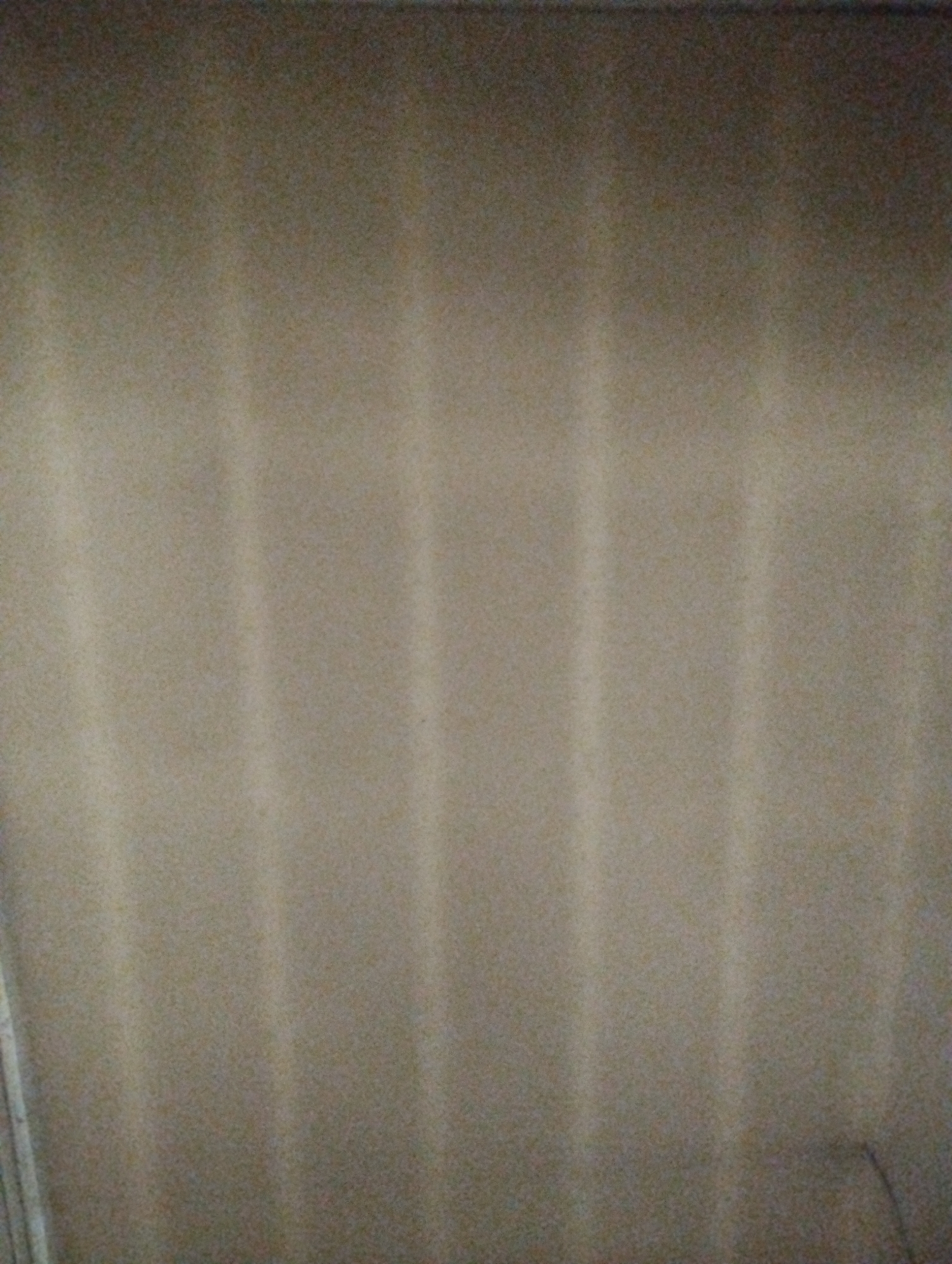 The image is a close-up, high-angle shot of a brown textured surface, likely a fabric or carpet, with vertical light and dark stripes. The stripes are subtle and appear to be a result of light reflection or the material's nap. The lighting is dim and casts a shadow on the right side of the frame, suggesting the light source is from the left. The overall texture of the surface is grainy. There are no people or objects clearly identifiable in the image. The location is unknown.