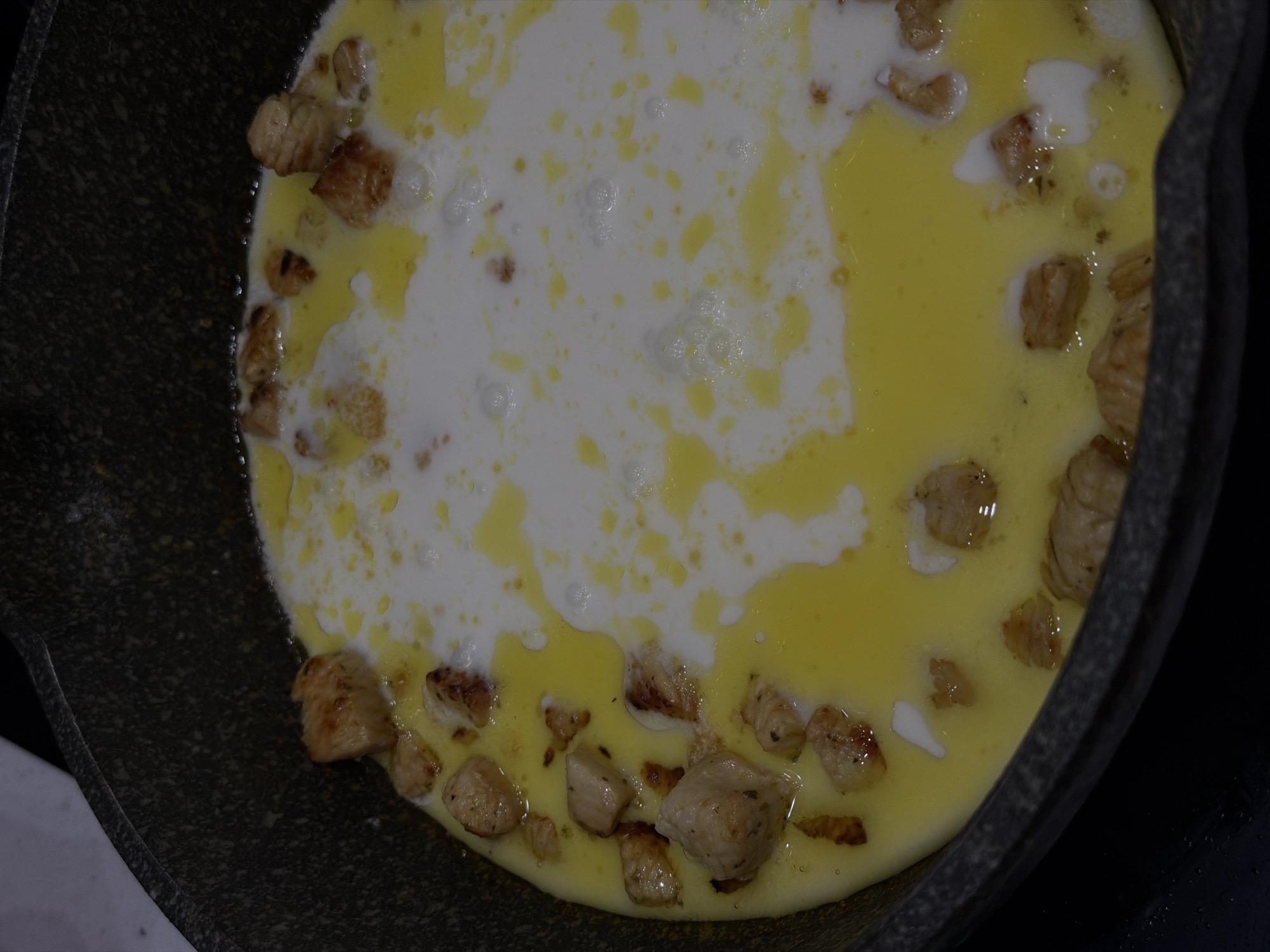 The image depicts a close-up view of a frying pan, likely made of cast iron, containing a cooking dish. The dish appears to consist of egg yolk and egg white mixture, with pieces of cooked meat, possibly chicken or pork, scattered around the edges of the pan. The dish is in the process of being cooked, indicated by the liquid consistency and bubbling in the center. The image doesn't provide enough information to determine the location in Khimki, Russia, or details about any people or interactions.