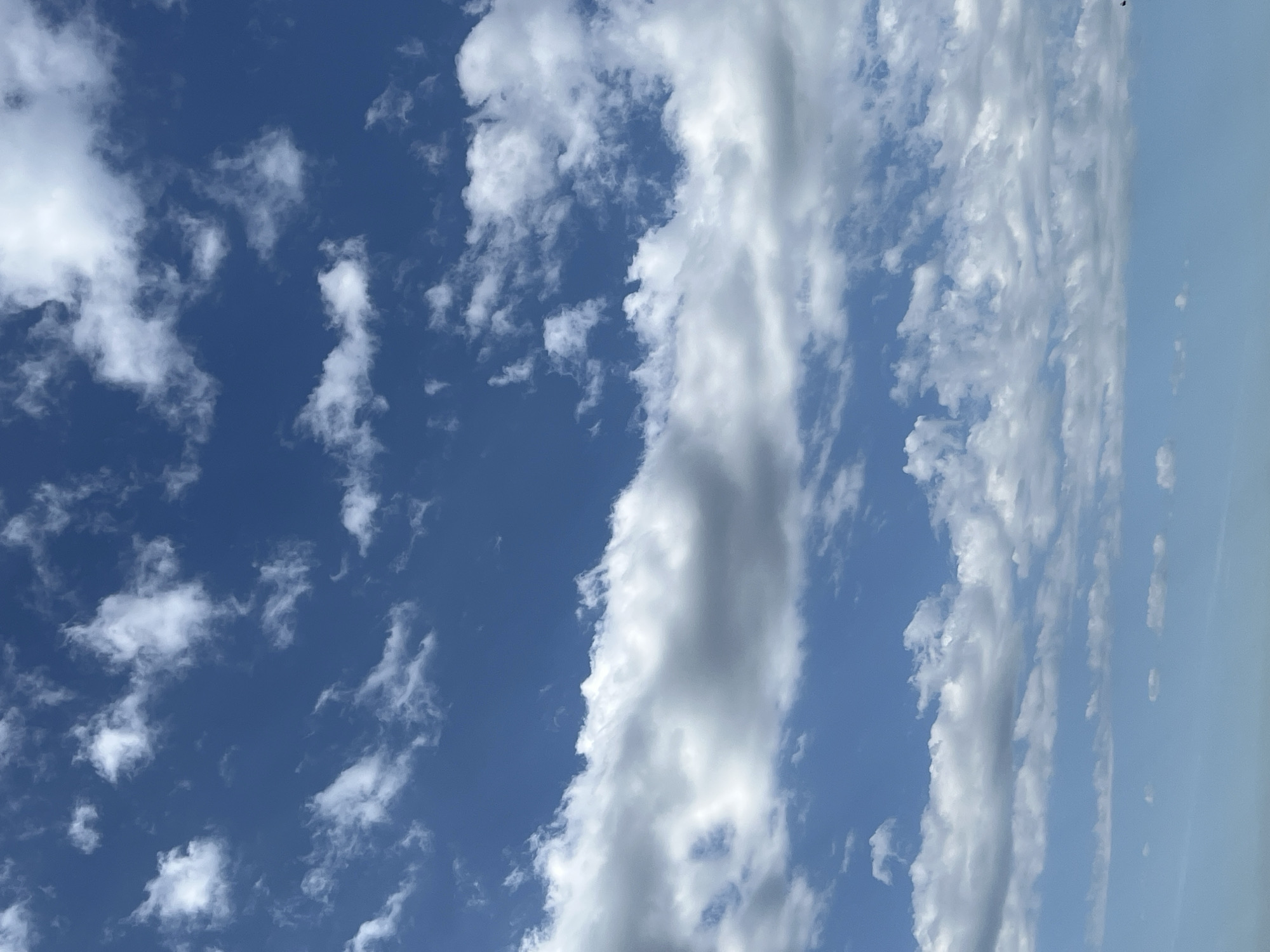 The image shows a view of the sky. The sky is blue with scattered white clouds. Some of the clouds are small and fluffy, while others are long and streaky. The location of the scene is not evident from the visual data.
