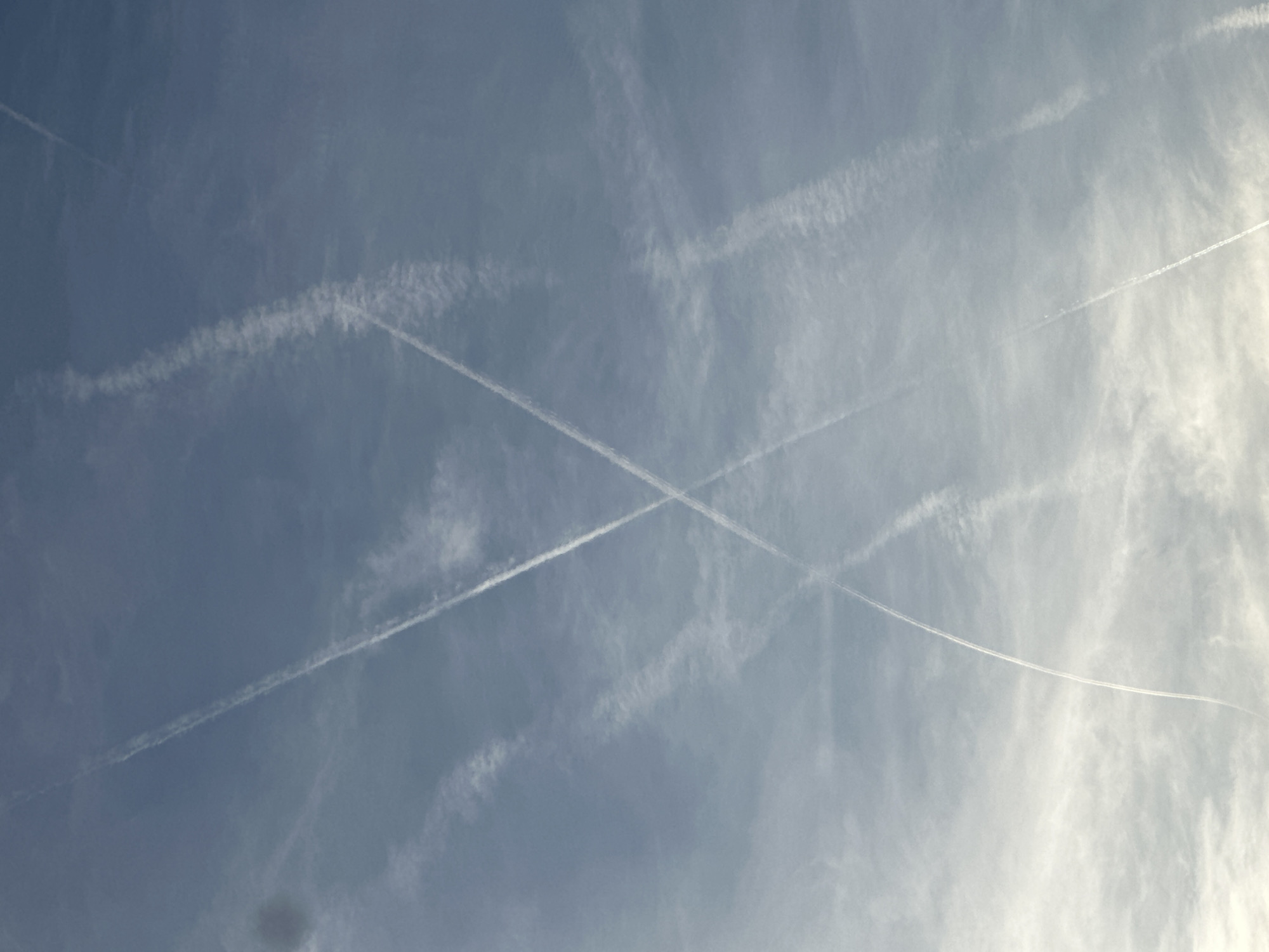 The image shows a blue sky with contrails. The contrails are crisscrossing each other. The location of the image is not indicated and cannot be discerned from it. There are no people, subjects, objects, actions, or interactions visible in the image other than the contrails. The environment is limited to the sky.