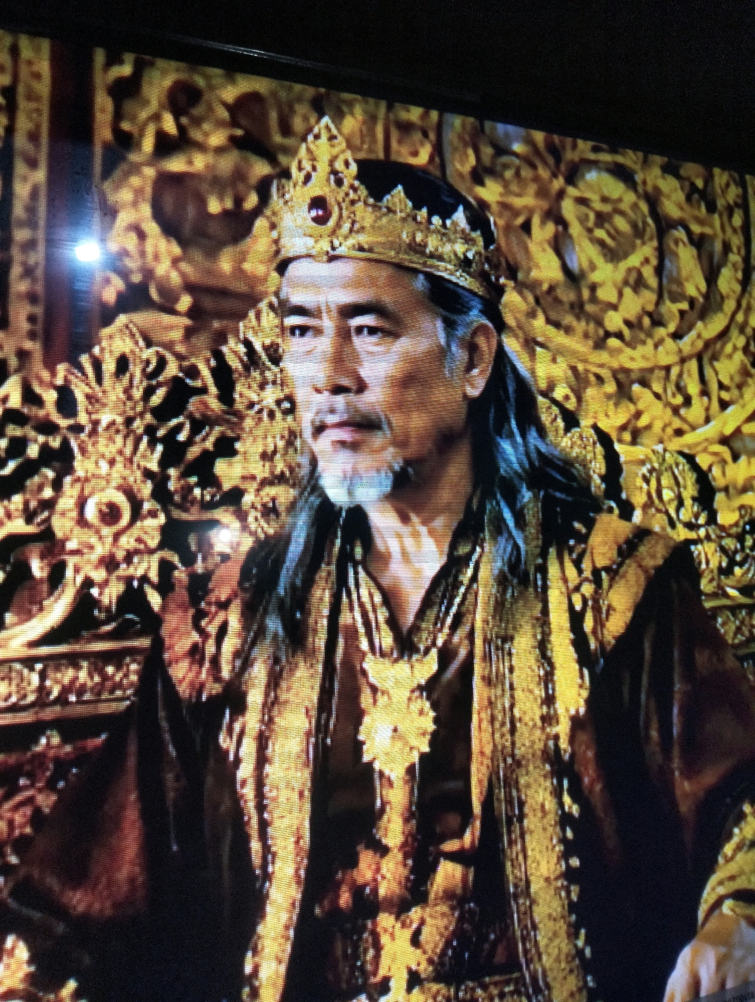 A man with long, dark hair and a goatee, wearing a golden crown and ornate, dark red and gold robes, sits on a golden throne. The background is elaborately decorated with golden, intricate patterns. This image does not depict a location in Semarang, Indonesia.