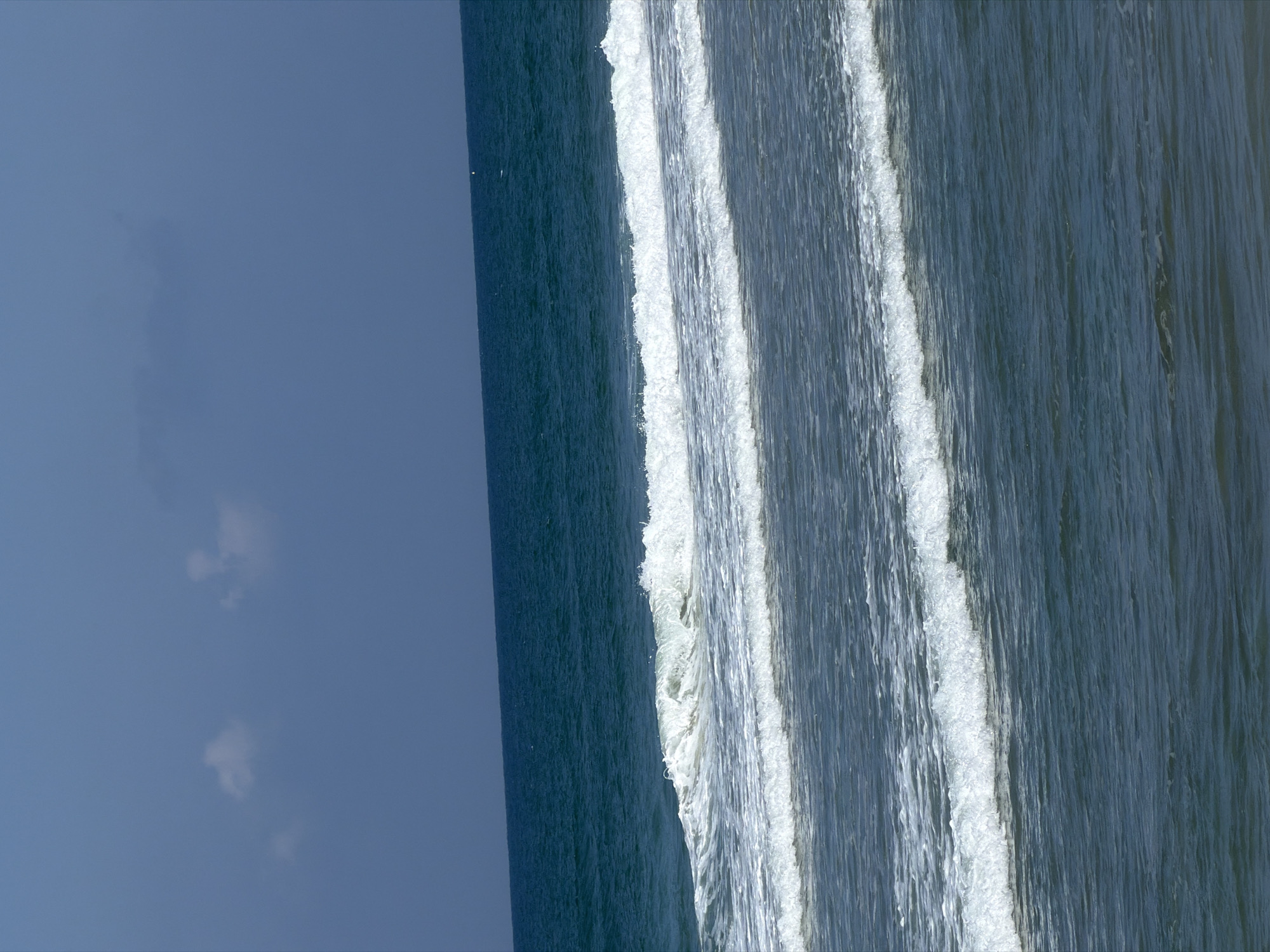 The image depicts an ocean scene with the sky occupying the left portion of the frame. The water is a dark blue-green with white foam from waves. There are multiple waves visible, creating parallel lines across the water. There is no visible land, people, or objects besides the sky and ocean. The location is Kiryat Yam, Israel.