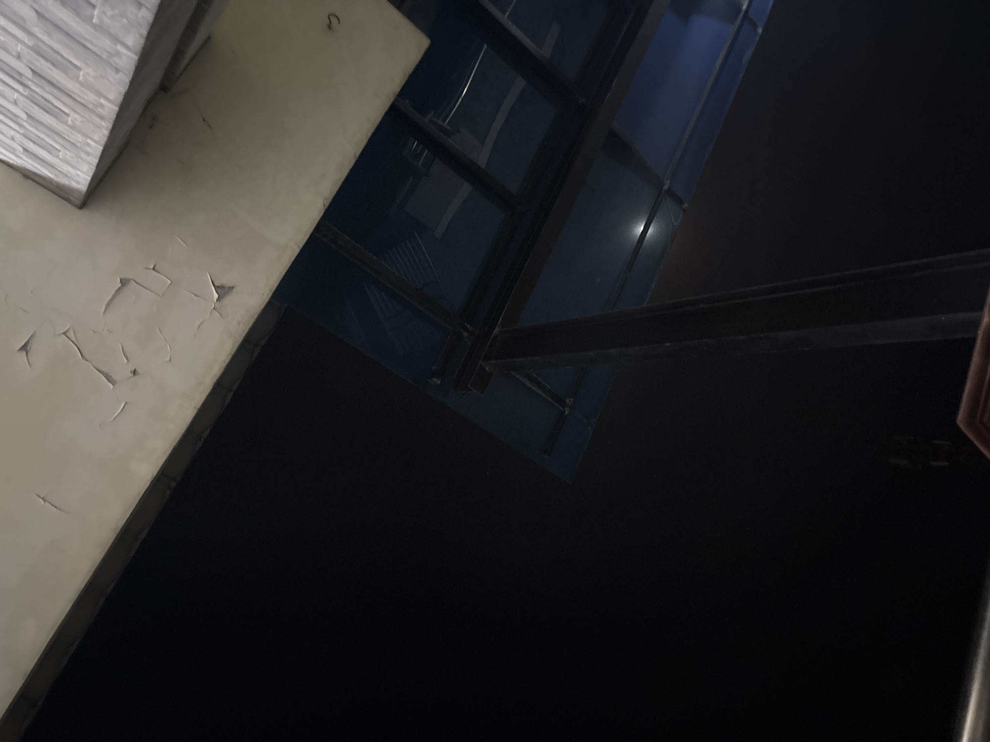 A low-angle, eye-level shot shows a dark sky with a partially visible structure. The structure consists of a light-colored overhang with peeling paint, a blue canopy supported by dark metal beams, and a metallic rectangular element at the top right. The lighting is dim, suggesting it is nighttime. The scene appears to be an outdoor area, possibly a bus stop or a covered walkway. No people or specific landmarks are visible to confirm the location in Gempol, Indonesia.