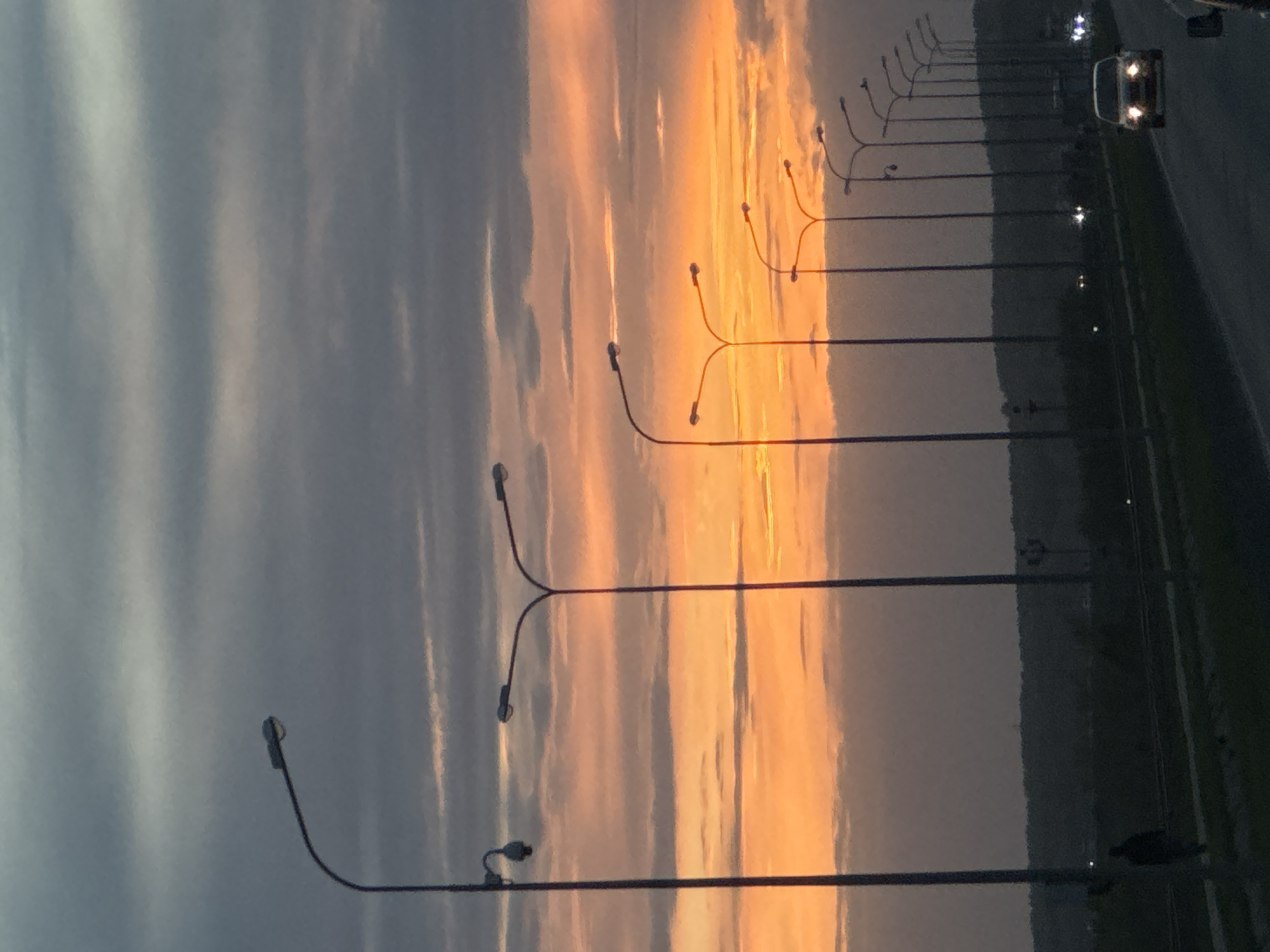 The image shows a sunset over a road, with a line of street lights. A car is visible on the road. The location is Chaikovsky, Russia.