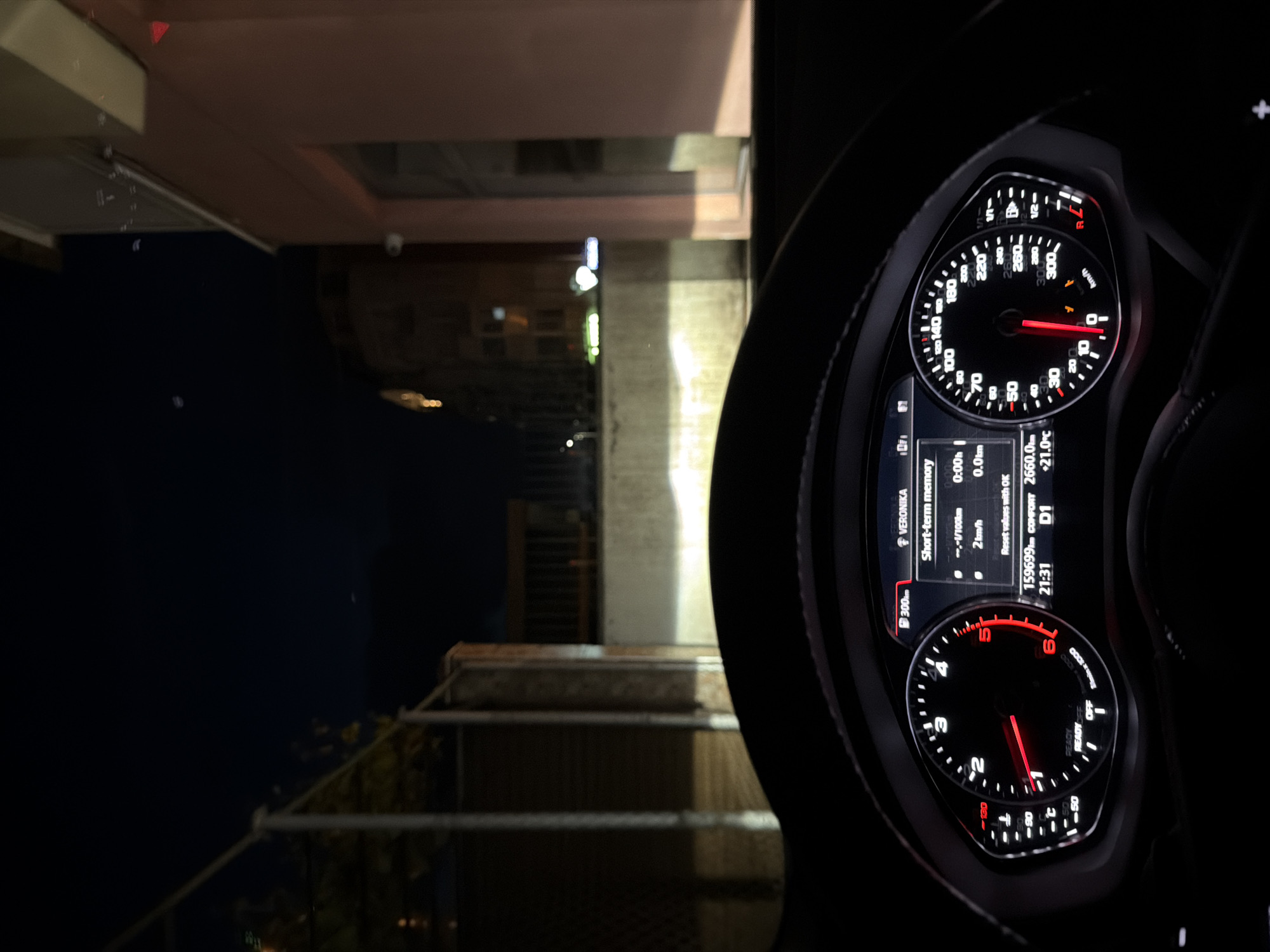 The image shows the interior of a car, specifically the dashboard and instrument panel. The speedometer indicates a speed close to zero, and the tachometer shows the engine is running at approximately 2000 RPM. The odometer reads 159699 km, the trip meter shows 2660.0km. The display shows a temperature of +21.0°C. The surrounding environment visible through the windshield appears to be a nighttime urban scene, showing the urban buildings. The location is assumed to be Burgas, Bulgaria.