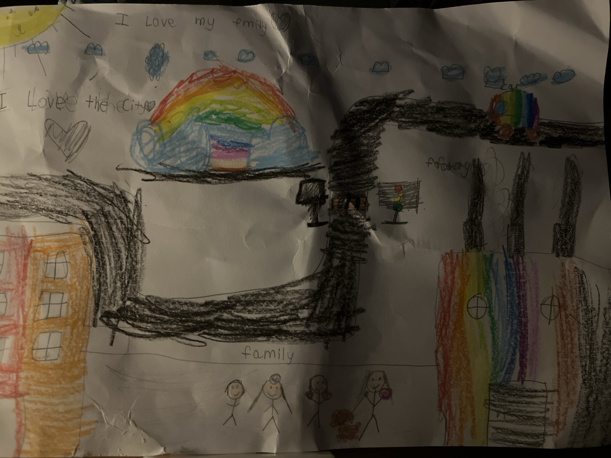 A child's crayon drawing depicts a cityscape. The top left corner features a yellow sun with a face and the text "I love my family" and "I love the city". A rainbow is above what appears to be a shelter or building. To the right, a black road leads to a rainbow-colored car and a "factory". Below, a stick-figure family is labeled "family". An orange and red building is to the left, and a rainbow-colored and grey building with three smokestacks is to the right. The background is white. The location of Bac Nha Trang Ward, Vietnam is not depicted or identifiable within the image.