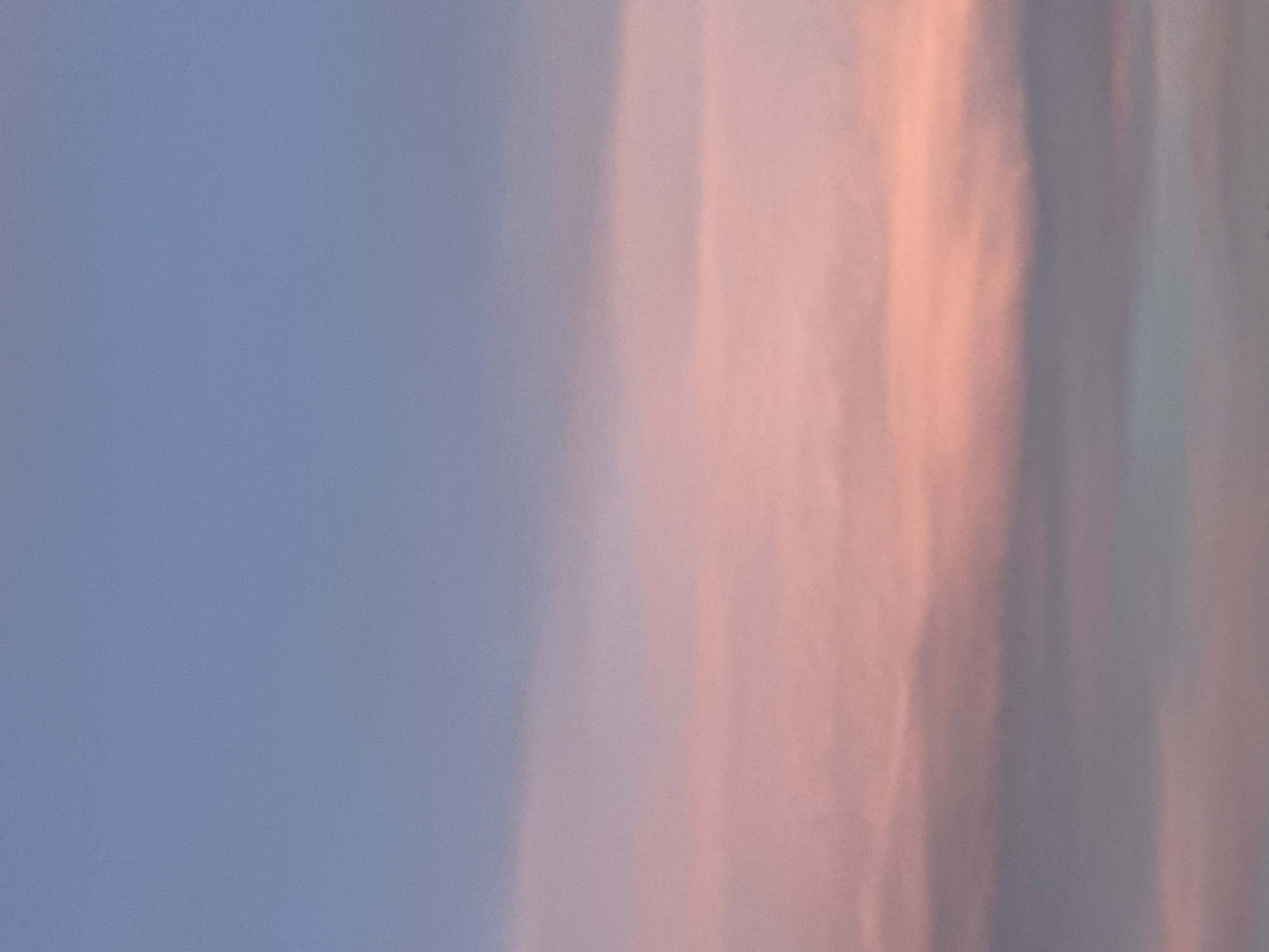 The image shows an abstract view of a sky during either sunrise or sunset. The left side of the image has a blue hue, while the right side has vertical streaks of light pink and grey. There are no identifiable people, objects, or landmarks to determine a specific location, including the city of Sofia, Bulgaria. The scene seems to focus on the color gradient in the sky.