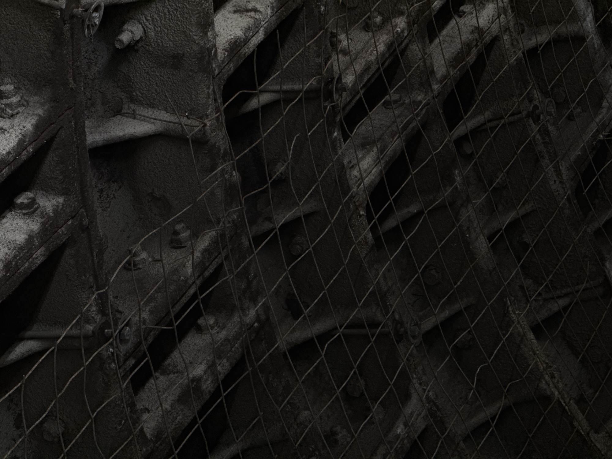 The image shows a close-up view of a dark, possibly industrial structure, partially covered by a wire mesh. The structure appears to be made of heavy, possibly metal or concrete components, fastened together with bolts. The overall scene is dark and grimy. It is not possible to infer the location as Moscow, Russia from this image alone.