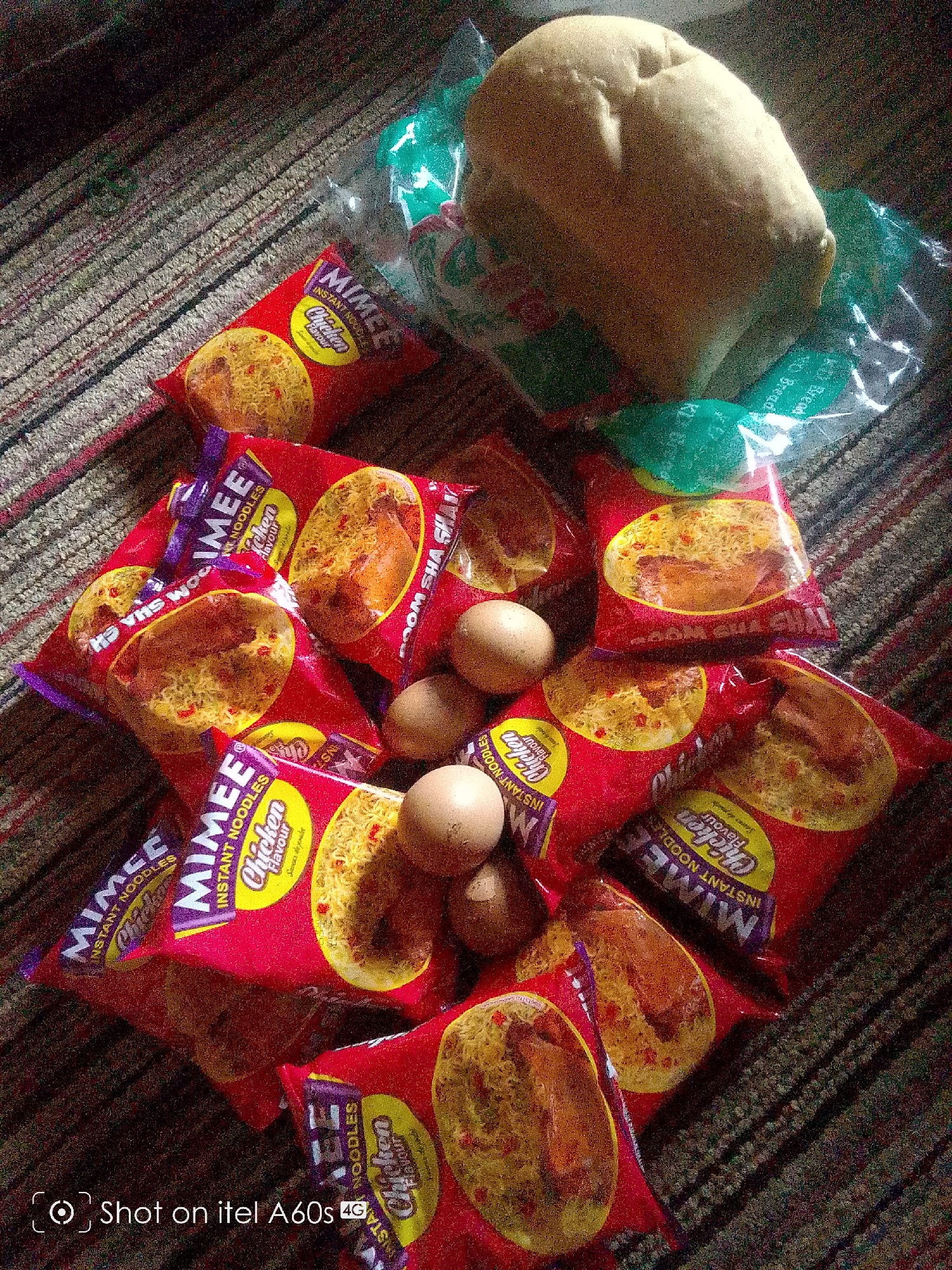 A loaf of bread in plastic wrap sits on top of a pile of instant noodles labeled "MIMEE Chicken Flavour" and three eggs. The products are positioned on a striped surface. The lower left of the image contains the text "Shot on itel A60s 4G".