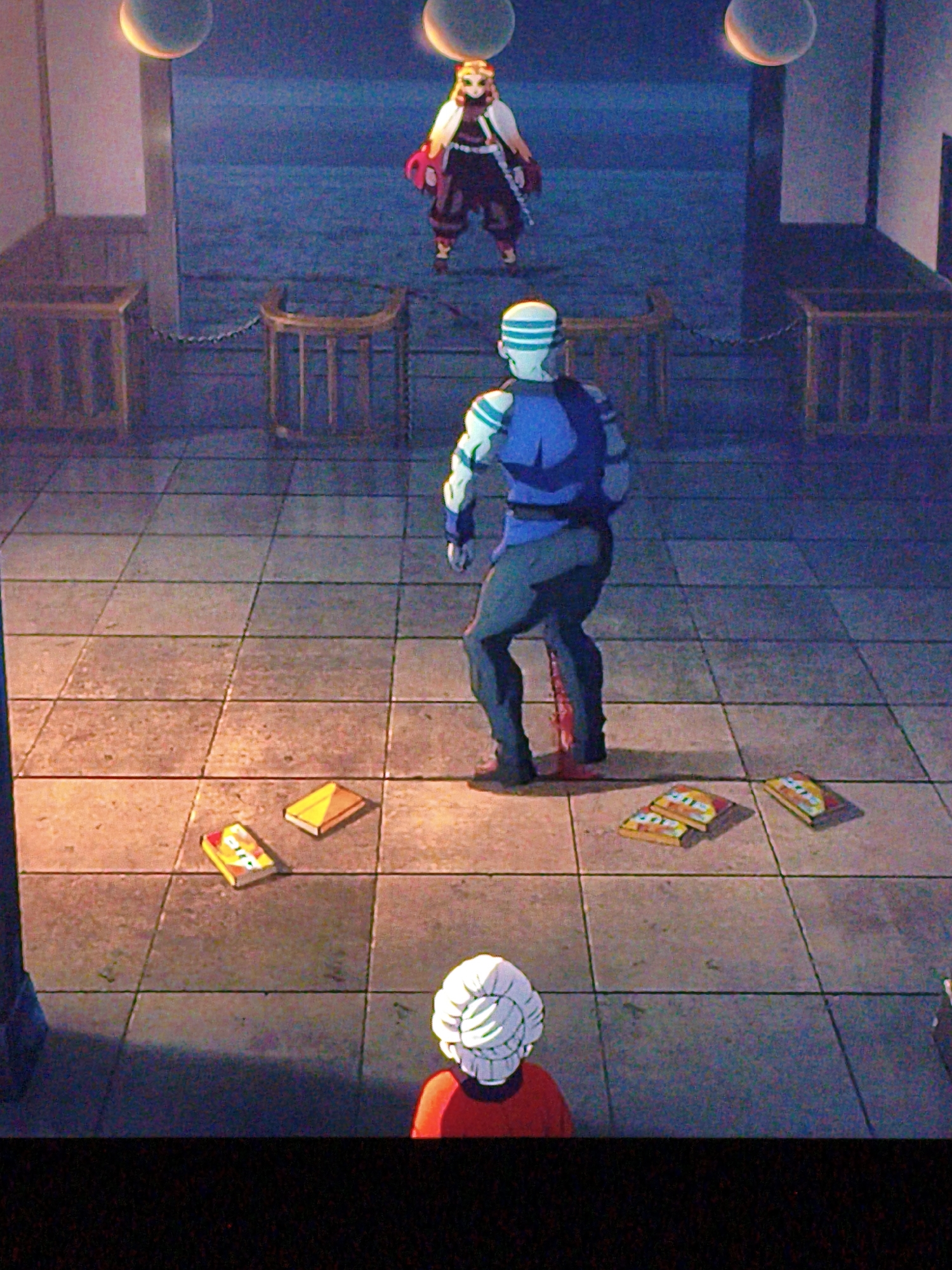An anime scene depicts an indoor courtyard with tiled flooring. Three individuals are present: a woman in a dark outfit with a white cape and red accents stands in the background; a man in a blue and white athletic suit with a white helmet stands in the mid-ground facing away from the viewer; and a person with white hair wearing a red shirt is in the foreground, also facing away. Scattered on the floor are several yellow and orange objects resembling books or boxes. Two wooden benches with curved backs are positioned in the mid-ground. The environment suggests an urban setting with architectural elements like columns and decorative spheres hanging from the ceiling, bathed in dim, artificial lighting. The scene does not contain any visual information that would place it in Vladivostok, Russia.