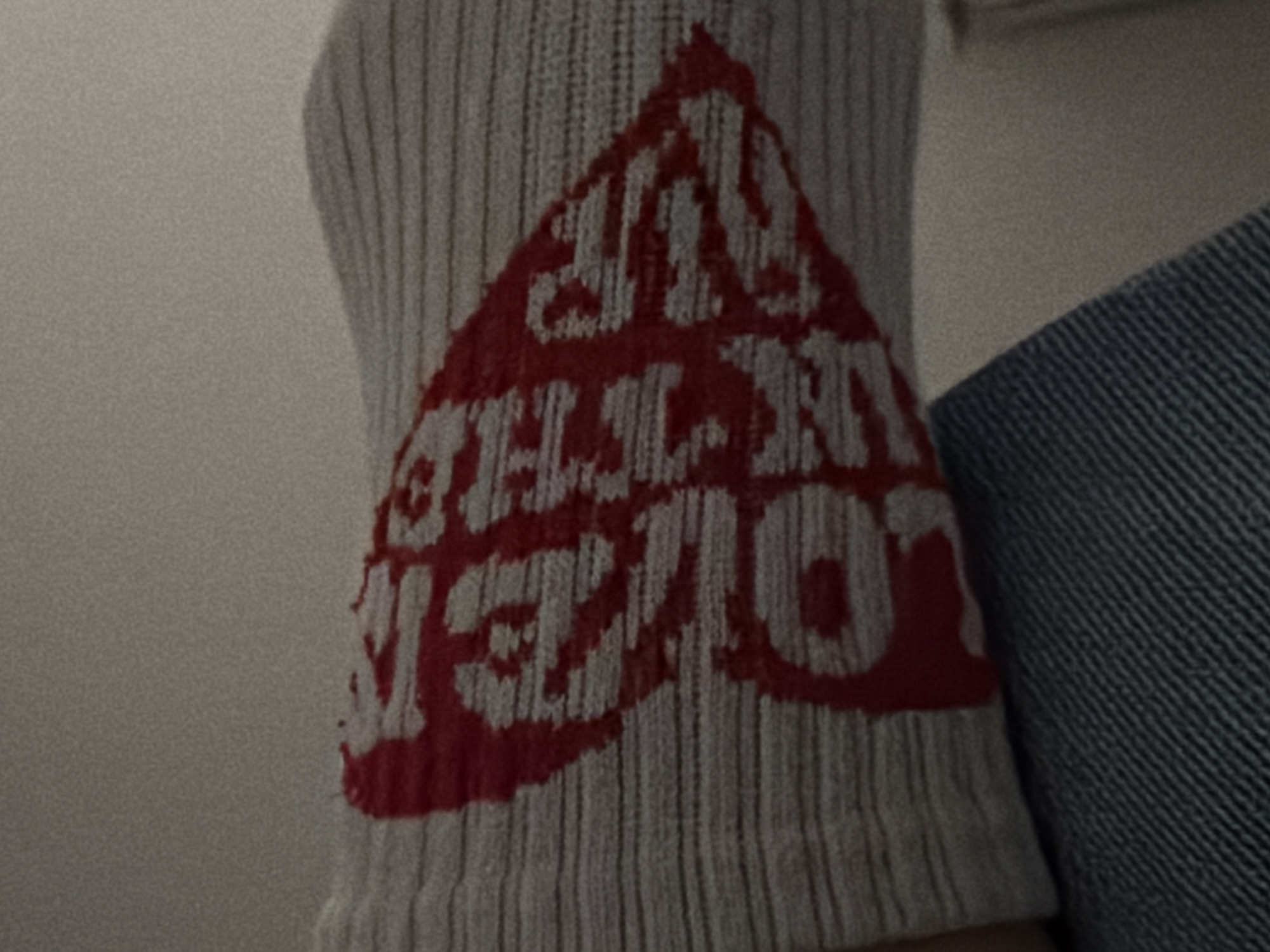 Close-up of a white ribbed sock with a red heart-shaped design containing the text "ALL MY LOVE IN THE RIP". The sock is positioned next to a denim-textured fabric. The background is a plain white wall. The location in Sofia, Bulgaria is not ascertainable from the available visual information.