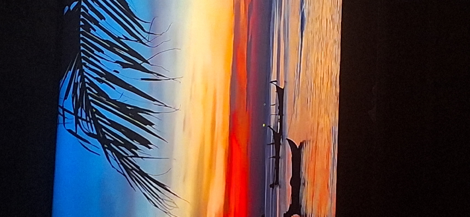 The image depicts a tranquil sunset scene over a body of water, possibly a sea or large lake. Silhouetted against the vibrant orange and red hues of the sunset are several boats, appearing to be traditional fishing vessels. One boat is closer to the foreground and appears to be a dugout canoe, while others are further out on the water. Above the horizon, a palm frond hangs from the top left corner of the frame, casting a shadow over the sky. The sky transitions from a deep blue at the top to fiery orange and red near the horizon, indicative of a dramatic sunset. The water reflects the colors of the sky, creating a shimmering effect. The scene is calm and serene. The image is a photograph of a painted or digitally rendered artwork and is not a real-world scene from Bila Tserkva, Ukraine.