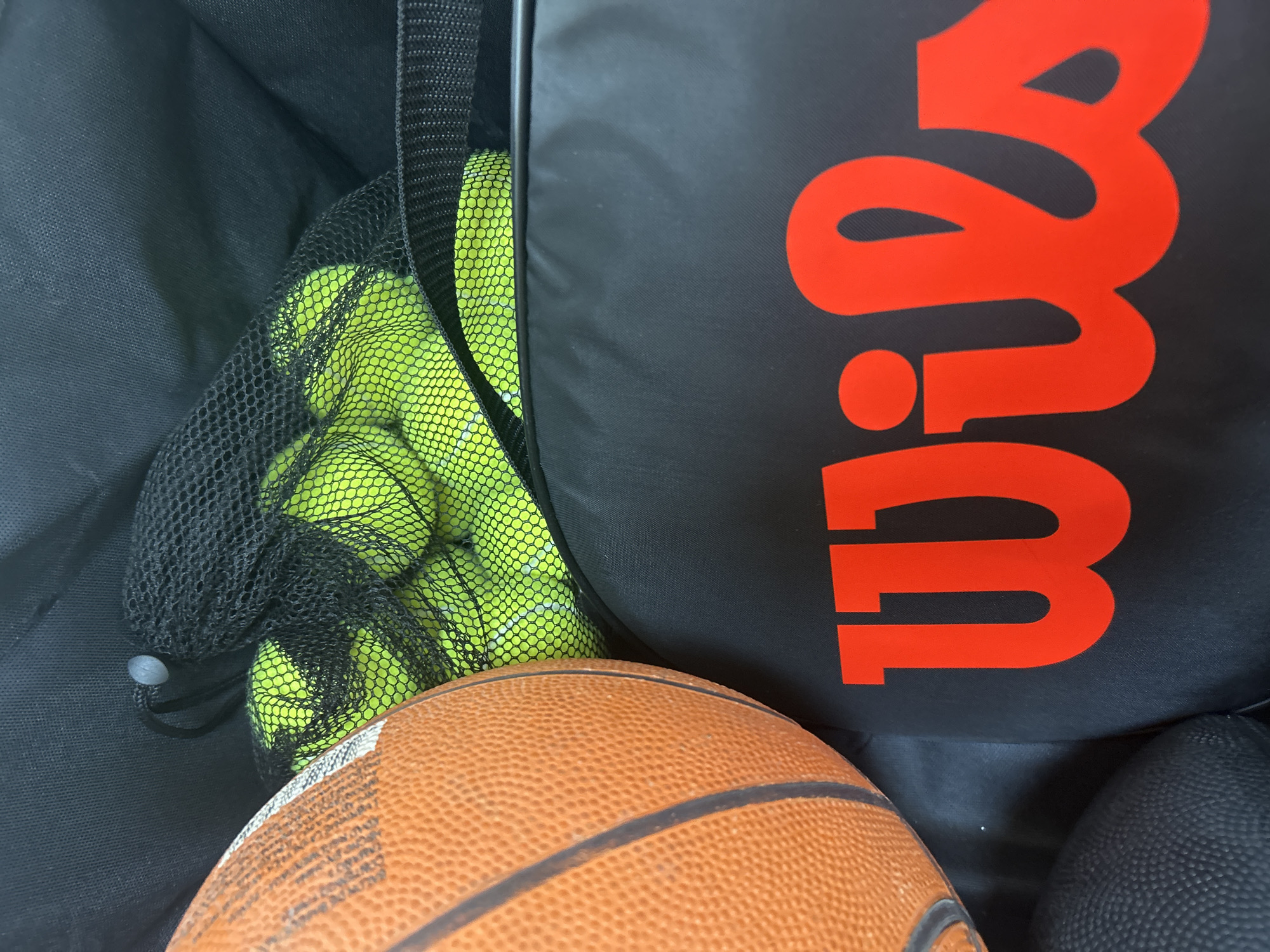 The image shows a black sports bag with a large red "Wilson" logo. Inside the bag, there is a mesh net filled with yellow tennis balls. The bottom of the image contains a brown basketball. In the lower right corner of the image, there is a black basketball.
I cannot determine the city and location in Mexico based on this picture alone.