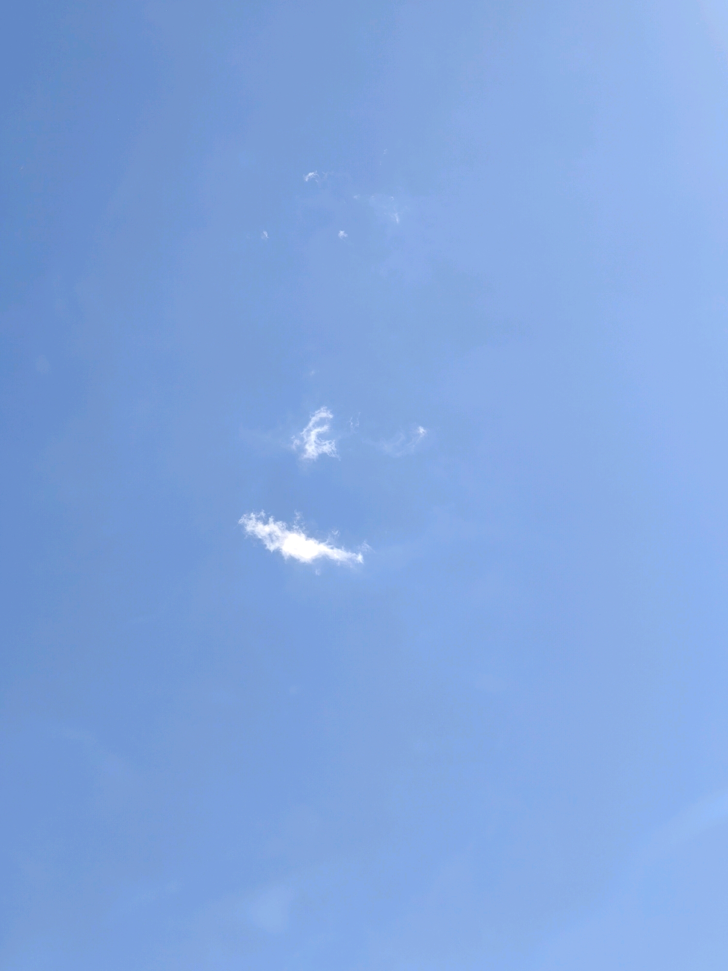The image depicts a bright blue sky with scattered white clouds. The clouds are small and wispy, with one larger cloud formation in the lower-left portion of the frame. There is no indication of the city of Karachayevsk, Russia, or any urban elements in the image. The scene is entirely focused on the sky.