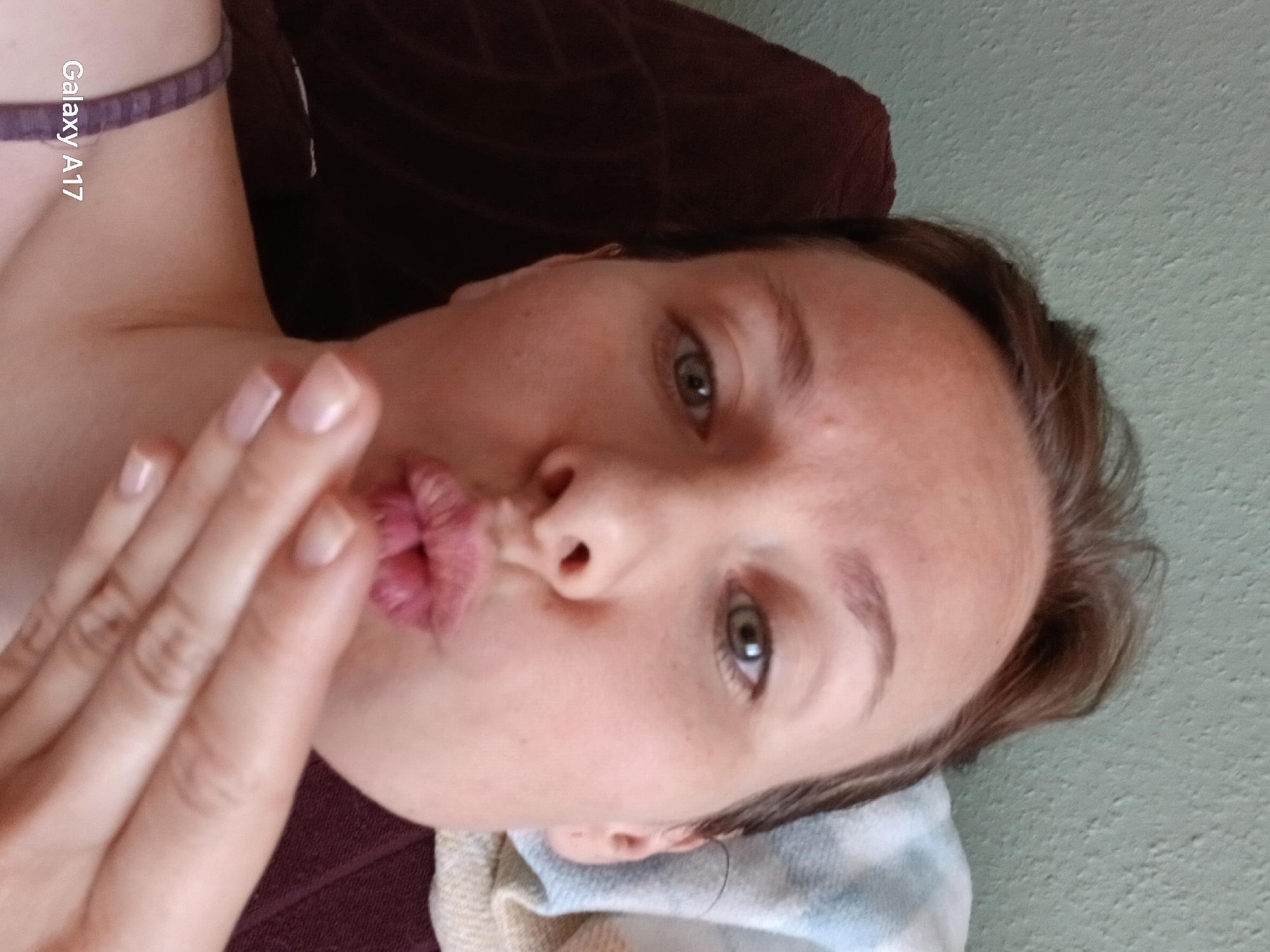 A woman is lying down, facing the camera. She has fair skin, light-colored eyes, and short brown hair. Her lips are pursed, and her hand is near her face. She appears to be resting on a brown couch or cushion, with a striped blanket or towel visible near her head. Part of her shoulder and a strap are visible. "Galaxy A17" is printed on the image. No information indicates the image was taken in Yekaterinburg, Russia.