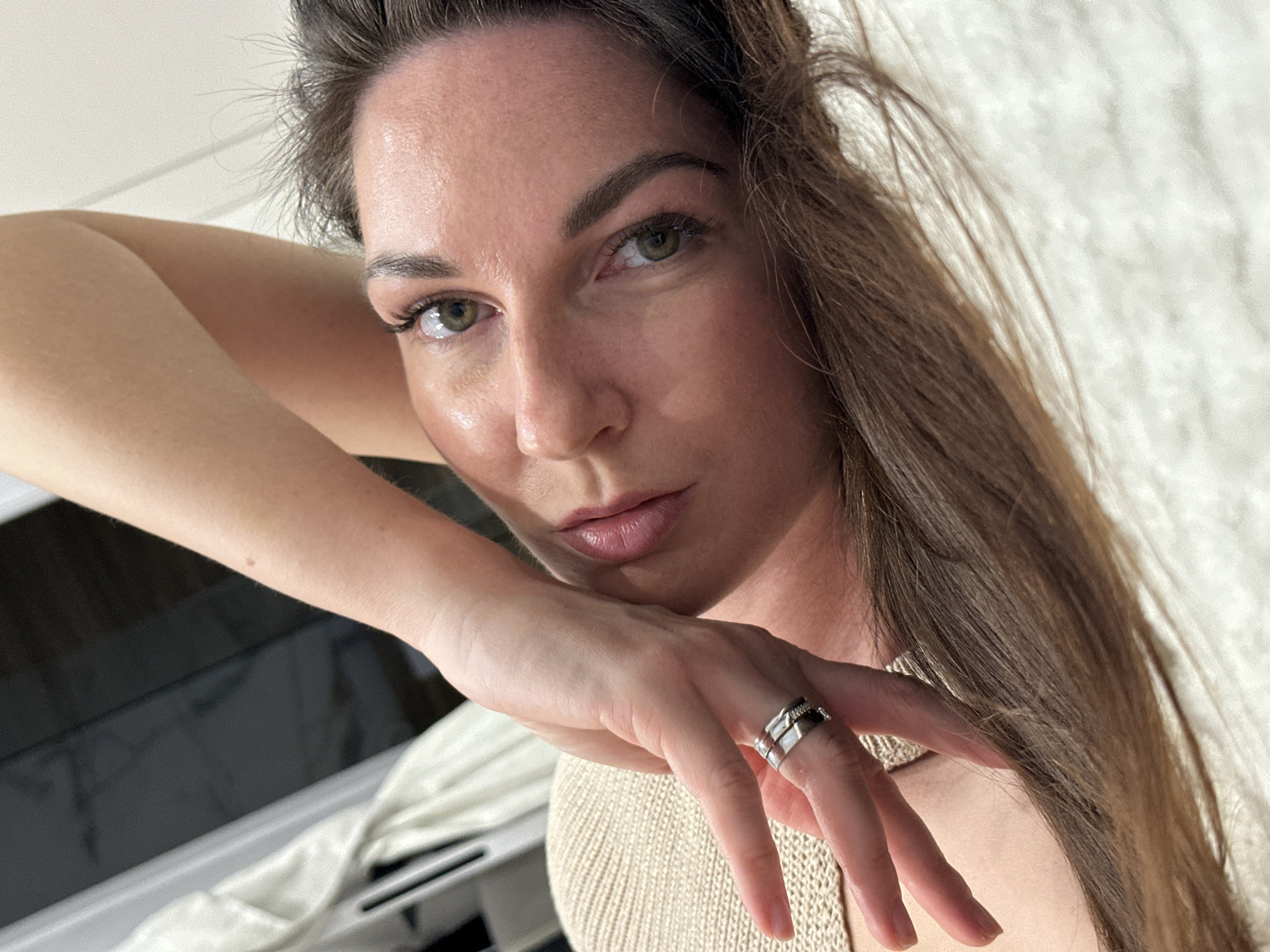 A woman with brown hair is shown in a close-up shot, wearing a beige knitted top and rings on her fingers. Her face is angled toward the camera, with a neutral expression. The background appears to be a lightly textured white surface. The image was likely taken indoors, but there is no way to ascertain the location of Chaikovsky, Russia, from this image.
