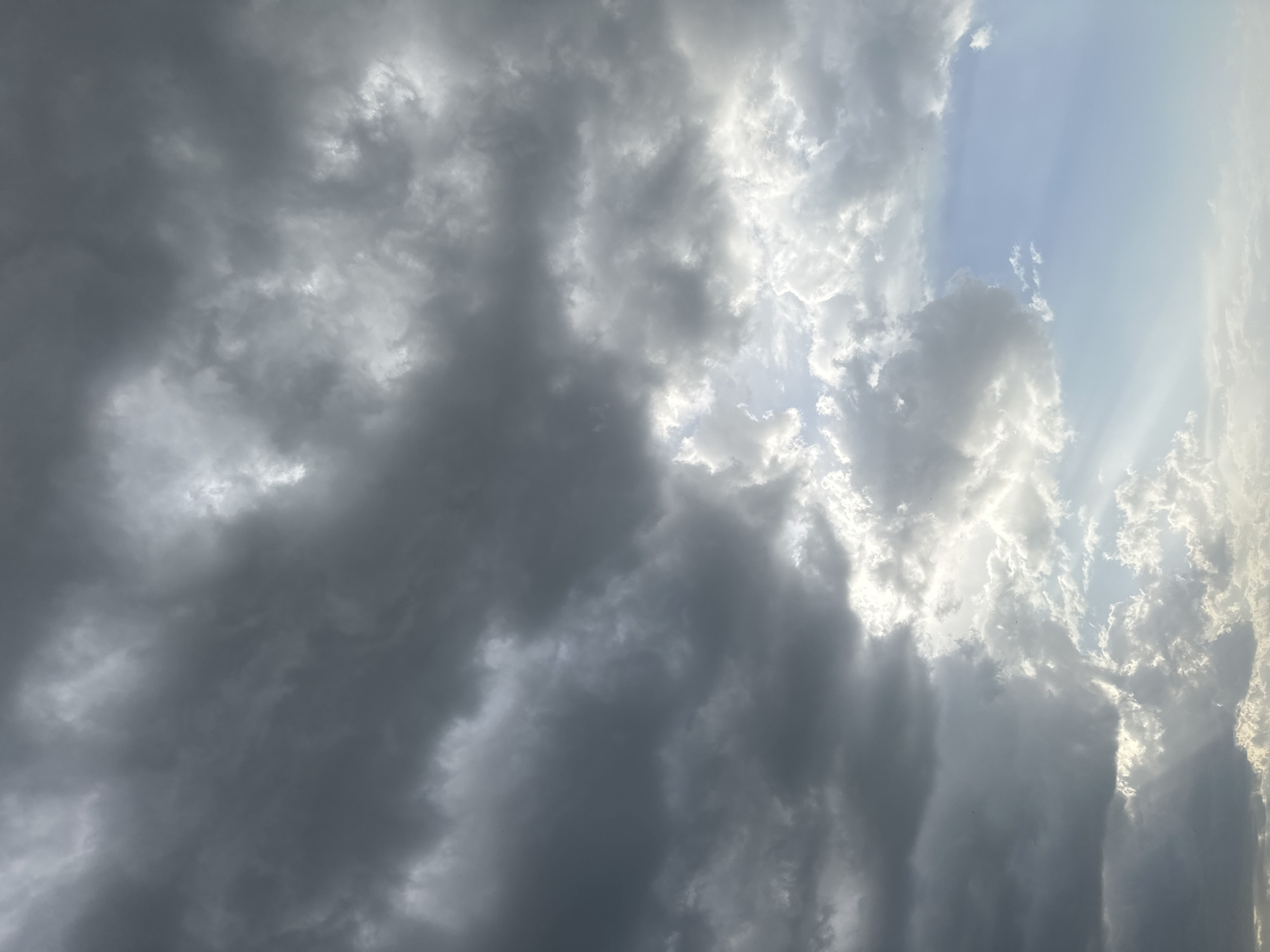 The image shows a sky filled with storm clouds. The clouds vary in shade from dark gray to light gray and white where the sun is breaking through. There is a small area of blue sky visible on the right side of the image. The clouds appear to be thick and heavy, suggesting an imminent storm. The location is not identifiable.