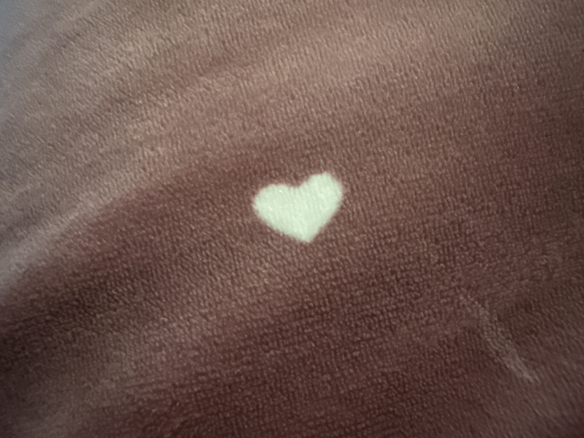 The image shows a close-up view of a textured, brown fabric with a small, light-colored heart shape in the center. The fabric appears to be soft and fuzzy, possibly velvet or velour. The heart shape is a distinct, lighter shade than the surrounding material, creating a contrast. There are no people or other objects visible in the frame. The background is entirely composed of this textured fabric. The specific location in the city of Bereznehuvate, Ukraine, cannot be determined from the provided image.