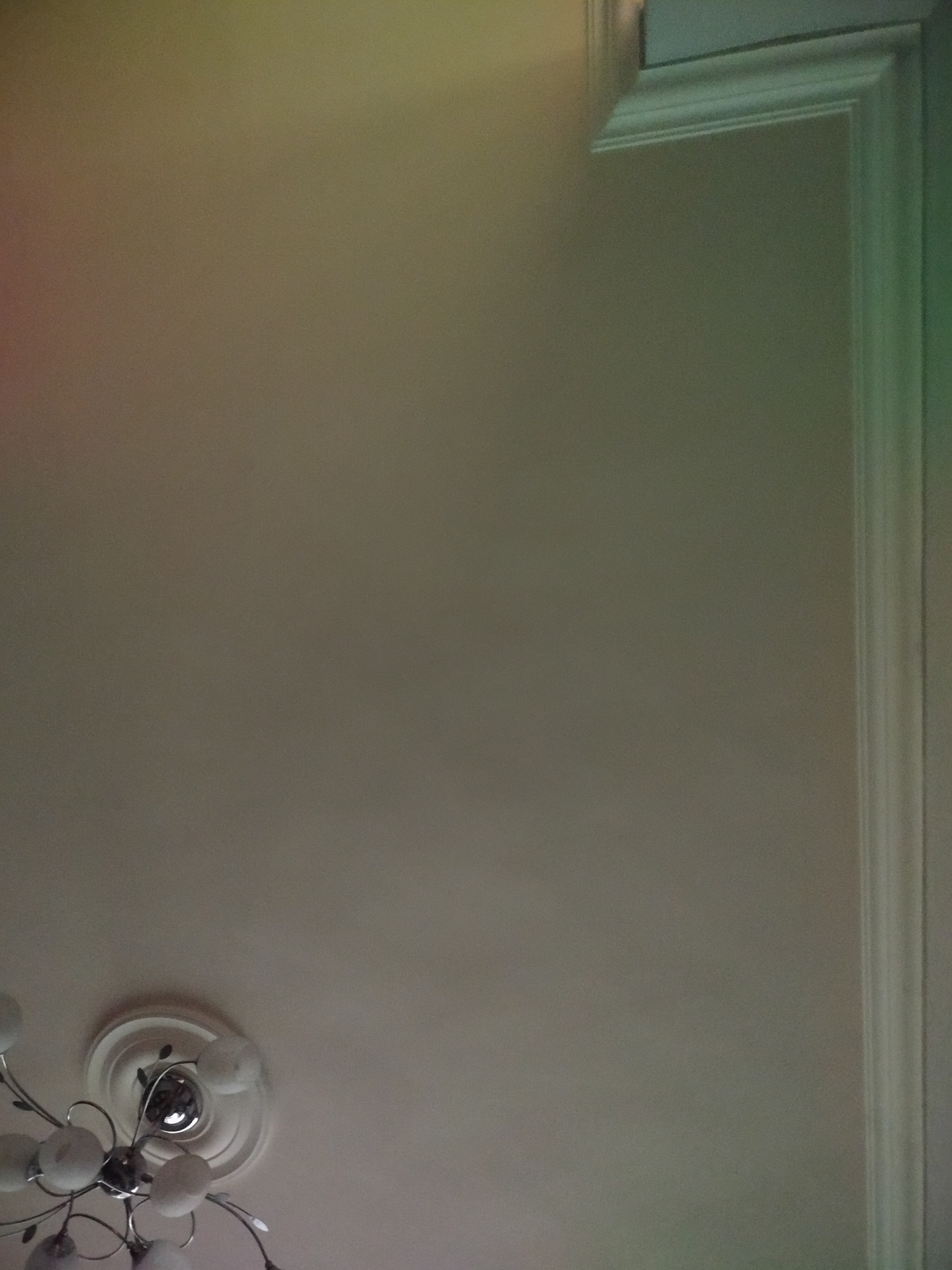 The image shows a ceiling with a light fixture and a decorative molding along the wall. The light fixture is white with multiple glass orbs attached to metal arms. The wall is a light color, and the molding is white with a detailed pattern. The image appears to be taken indoors. There is no identifiable city or people present.