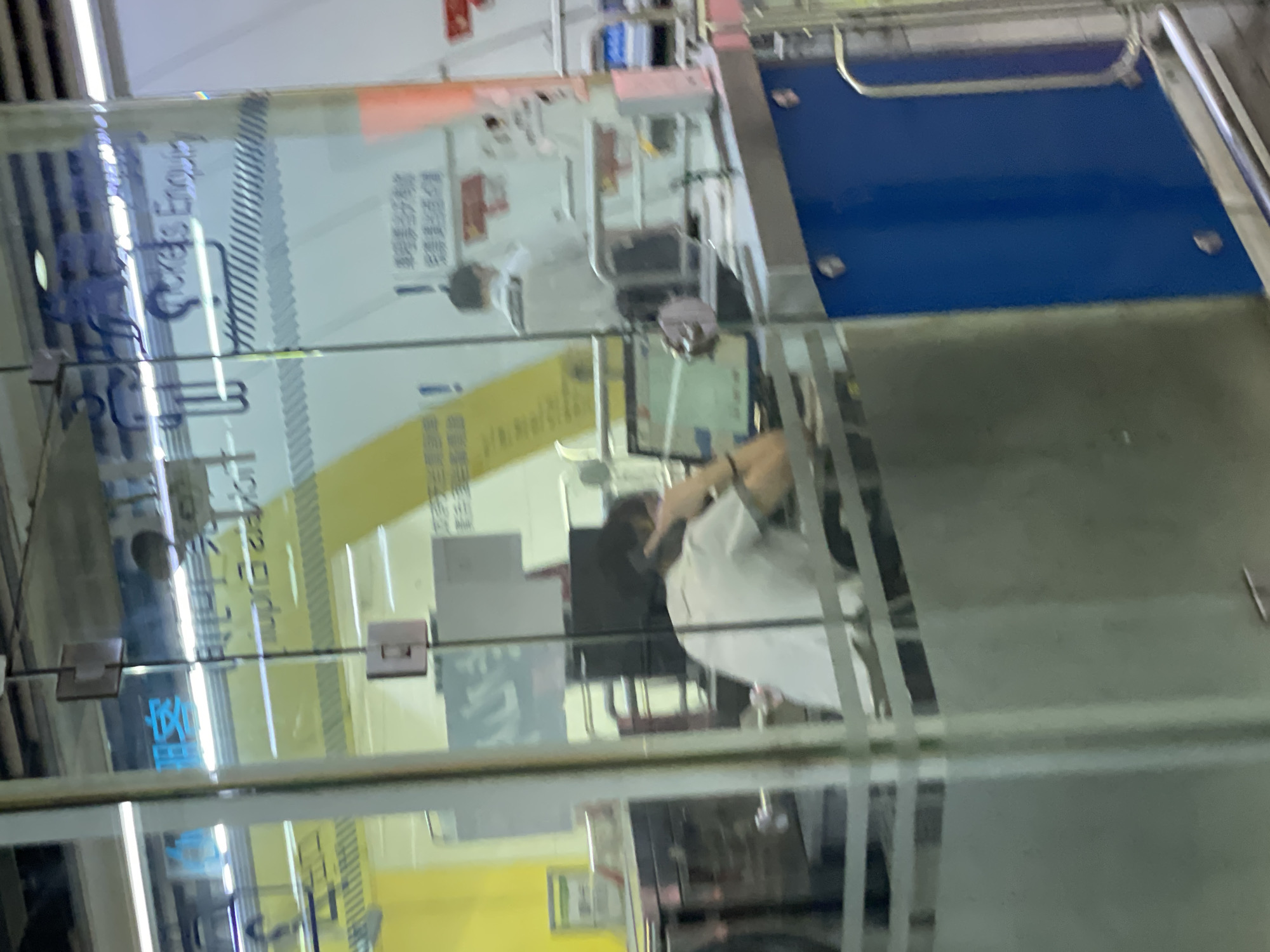 The image shows a glass window or door with the words "Tickets Enquiry" written on it. Inside, a person is visible, seemingly interacting with a desk or counter. The background suggests an indoor setting, possibly an office or service area. The image is a bit blurry, making it difficult to discern specific details of the environment.
