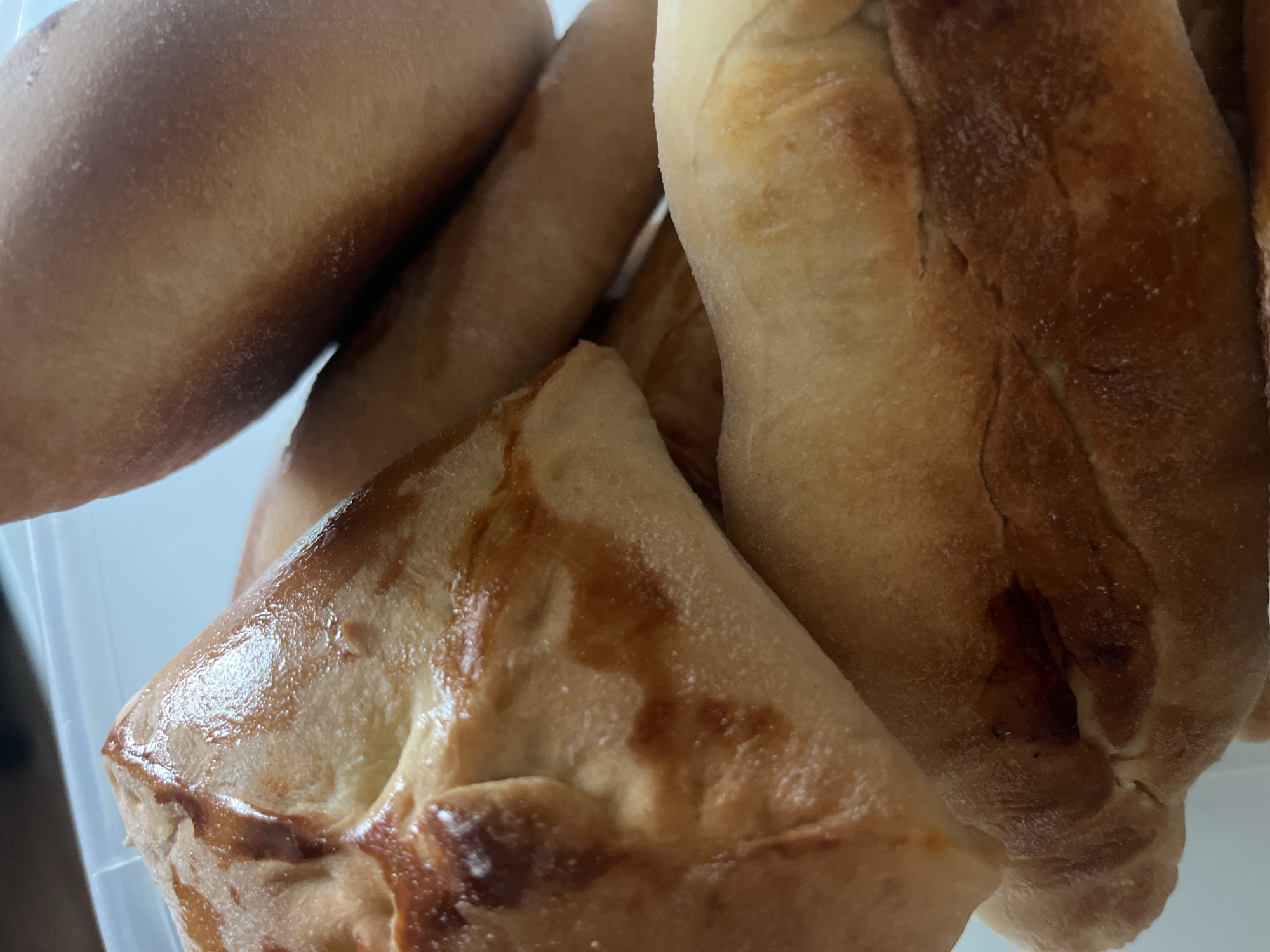 A close-up shot shows an assortment of baked goods with golden-brown crusts. Among them is a triangular pastry with a glazed surface. The pastries are likely in a container. There is no evidence in the image to confirm a location in Shushary, Russia.