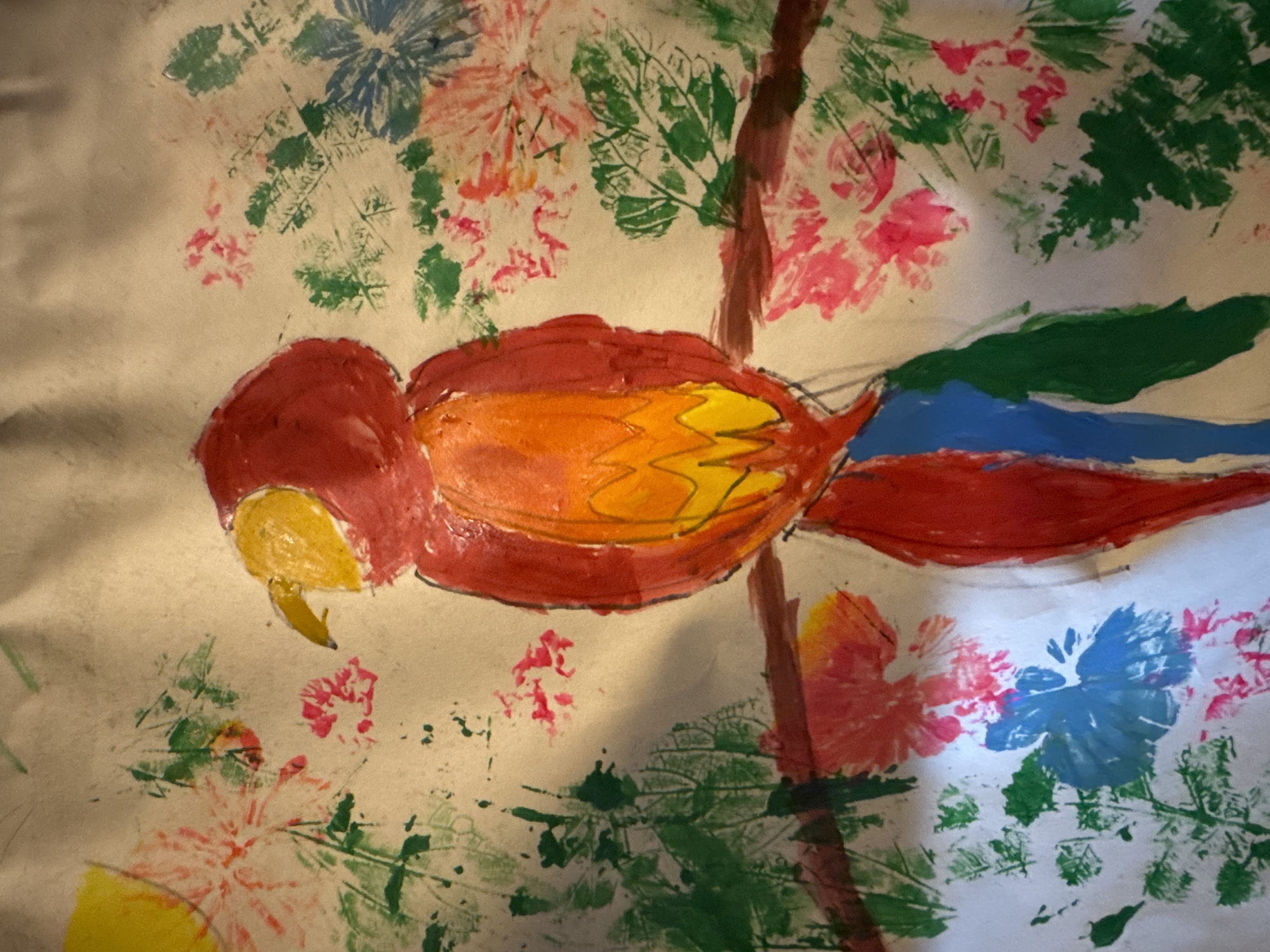 The image is a painting of a parrot perched on a branch, surrounded by floral and foliage designs. The parrot has a red head, a body with red, orange, and yellow sections, and a tail with red, blue, and green sections. The branch is brown. The background includes leaf and flower prints in various colors like green, blue, pink, and red. There is no information that allows me to know the location in Mèo Vạc Commune, Vietnam.
