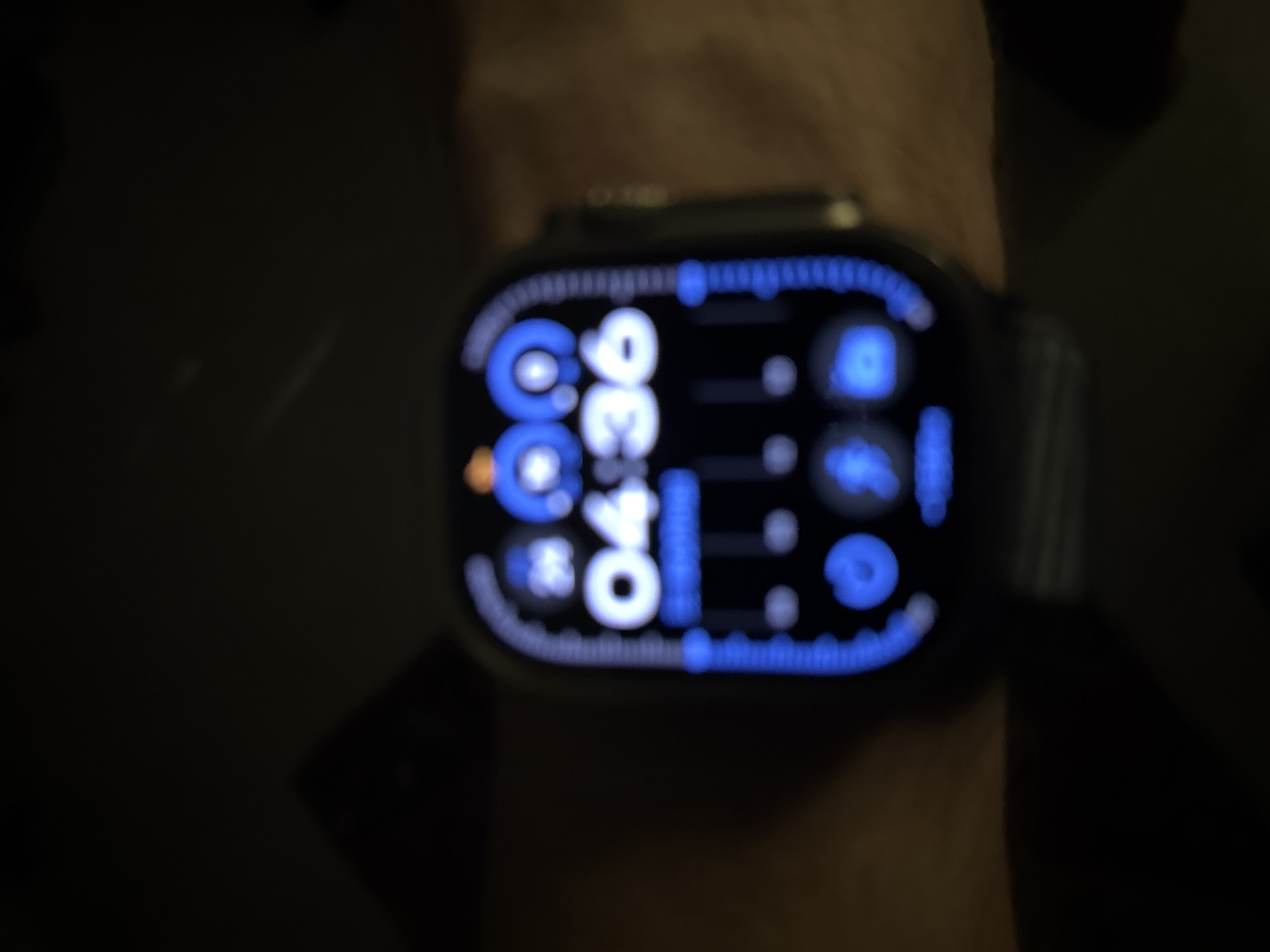 A blurry image of a person's wrist wearing an Apple Watch. The watch face displays the time "04:36" in white numerals on a black background with blue icons and a dotted perimeter. The watch is worn on the left wrist. The background is dark and out of focus. The photo was not taken in Lâm Viên - Đà Lạt, Vietnam.