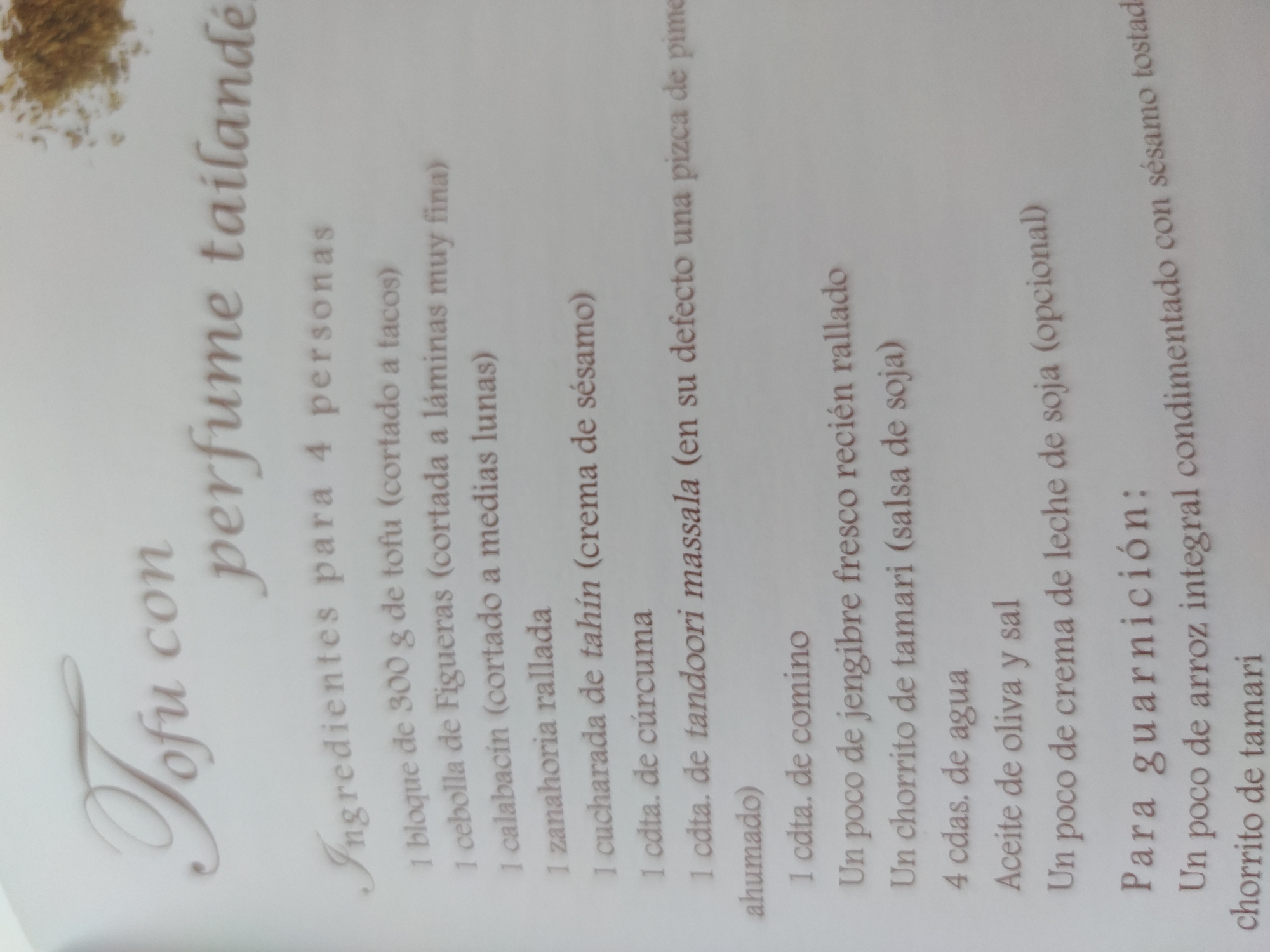 The image shows a page from a cookbook or recipe guide. The title of the recipe is "Tofu con perfume tailandé" (Tofu with Thai perfume), and it is intended for 4 people. Below the title are the ingredients and quantities needed for the recipe. These include tofu, figuera onion, zucchini, grated carrot, tahini, turmeric, tandoori massala, cumin, fresh ginger, tamari sauce, water, olive oil, salt, and soy cream. At the bottom of the page is the "Para guarnición:" (for garnish) section, which lists ingredients such as brown rice flavored with toasted sesame seeds and a dash of tamari.