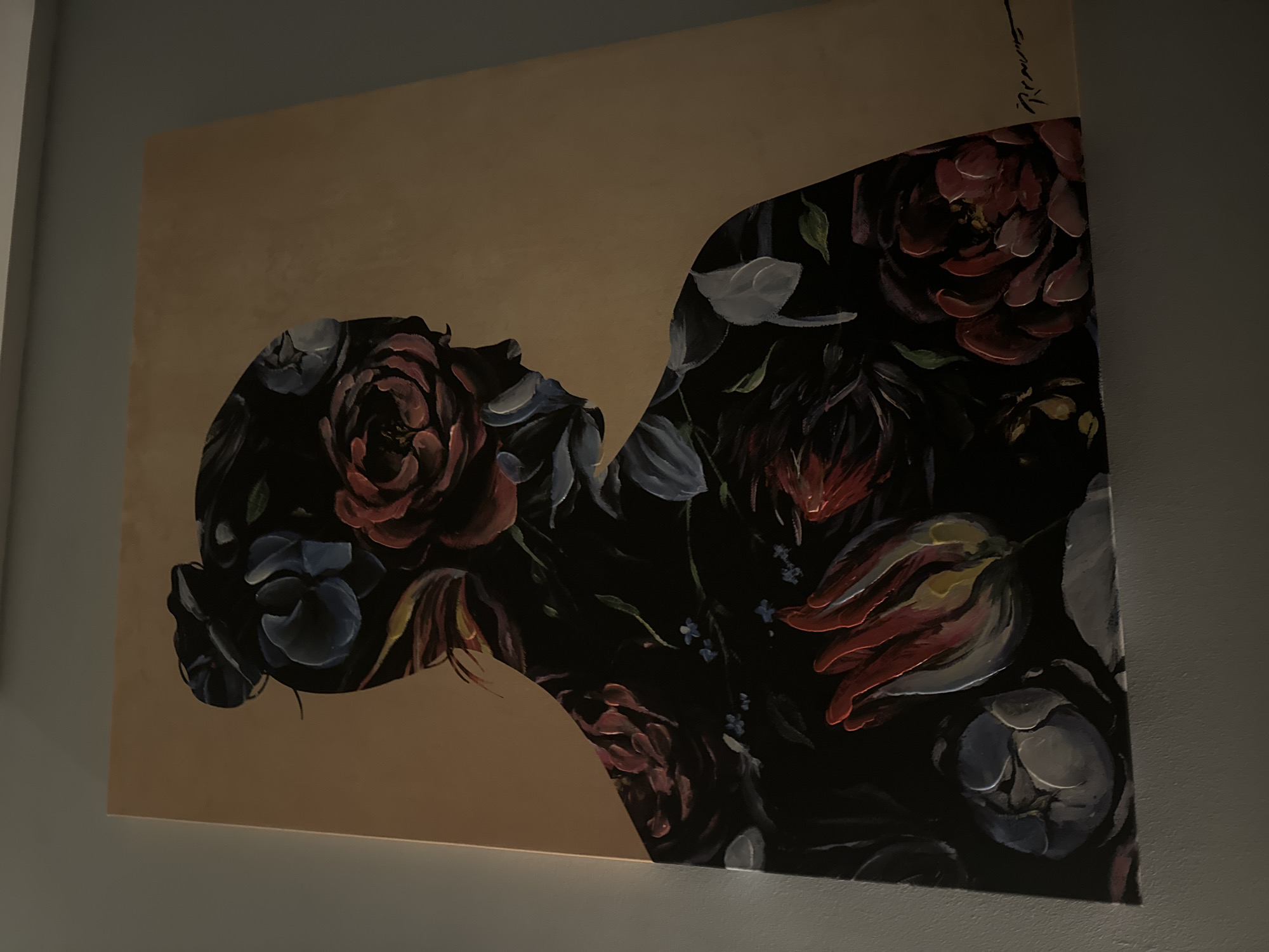 The image shows a painting hanging on a light grey wall. The painting depicts a silhouette of a person's head and torso filled with a dark floral pattern. The background around the silhouette is a muted tan color. There is handwriting visible in the upper right corner of the painting. The scene appears to be indoors, potentially in a home or gallery. There is no indication of the location being in Sofia, Bulgaria.