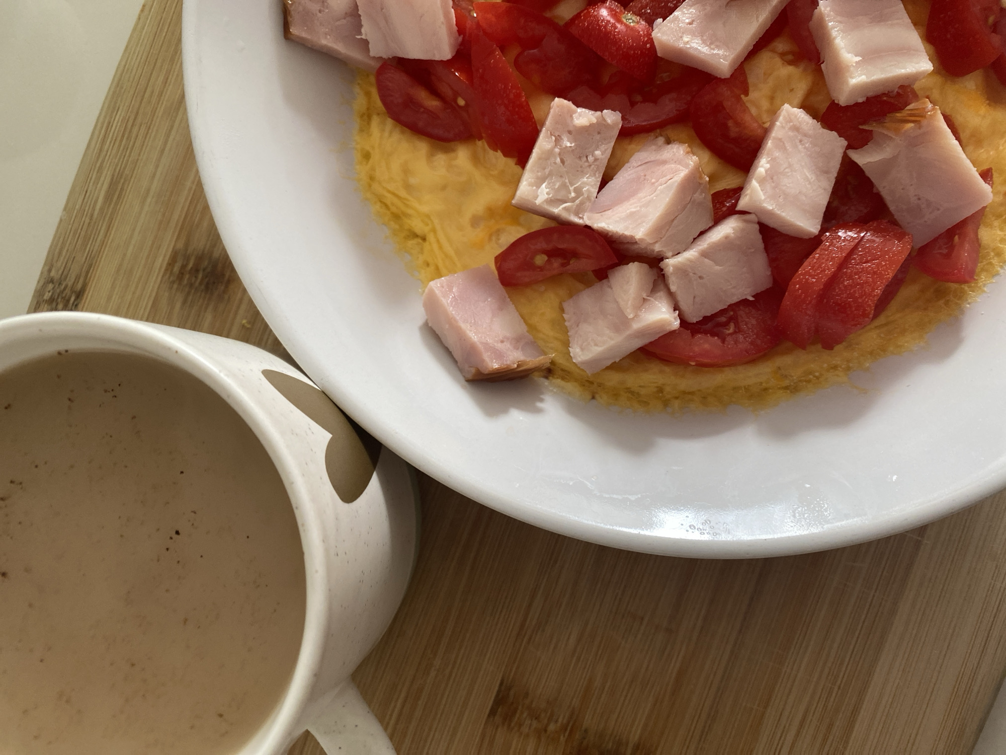 A close-up shot shows a breakfast meal and a mug of coffee on a wooden cutting board. The meal consists of an omelet topped with diced ham and cherry tomatoes. The mug, white with a heart design, is filled with coffee. The setting appears to be a domestic environment. There is no indication of location within Yanino-1, Russia.