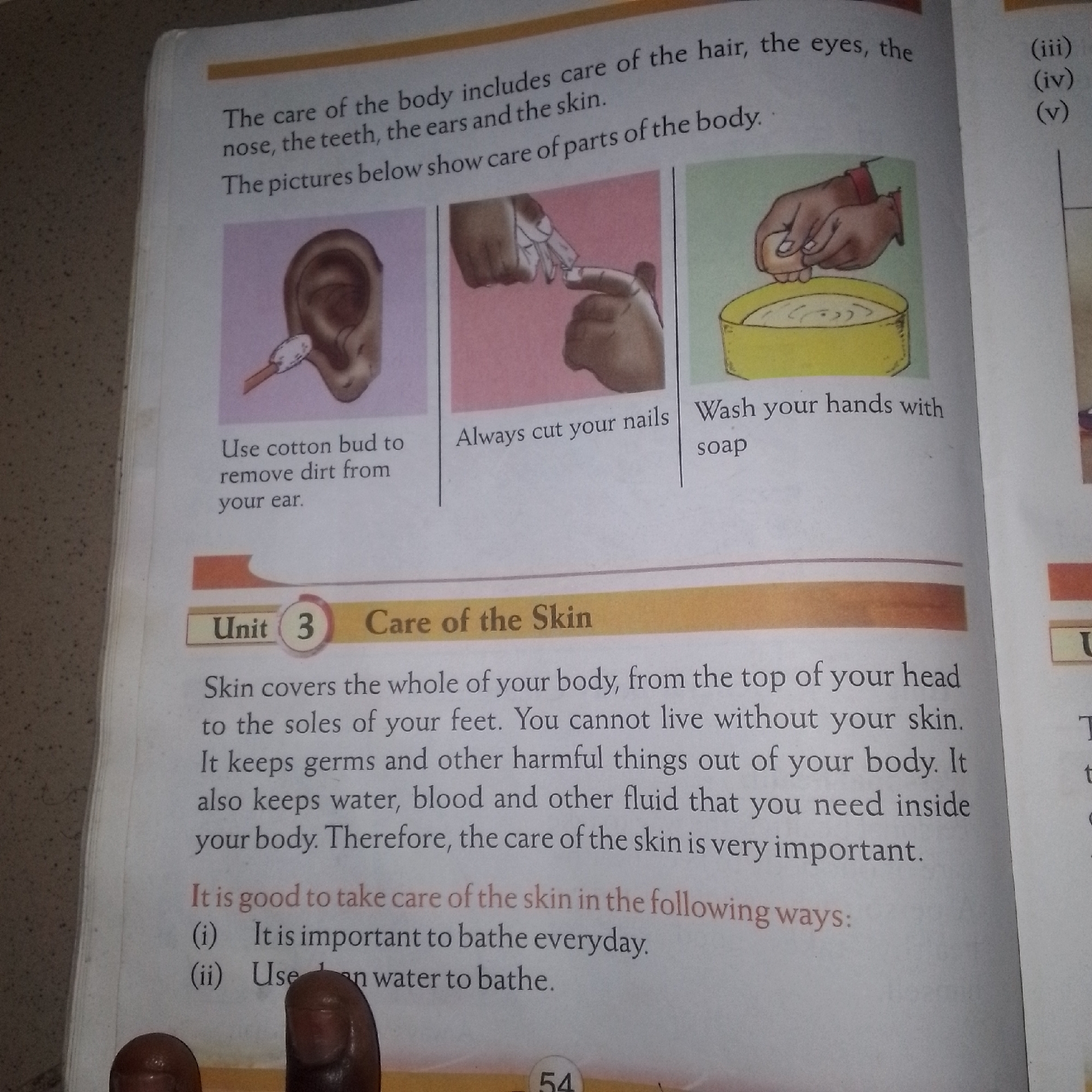 The image is a close-up, eye-level, interior shot of a book open to a page titled "Unit 3 Care of the Skin". The text discusses the importance of skin care, and is accompanied by three illustrations. The first illustration shows a cotton bud being used to clean an ear. The second shows hands trimming fingernails. The third shows hands washing in a yellow basin. Below these illustrations, the text continues with bullet points indicating ways to care for the skin, with the first two points partially visible: "(i) It is important to bathe everyday." and "(ii) Use warm water to bathe." The book's page number "54" is visible at the bottom center. The background is a blurred interior of what appears to be a room, with a speckled texture. The image does not contain any information about a specific city or location.